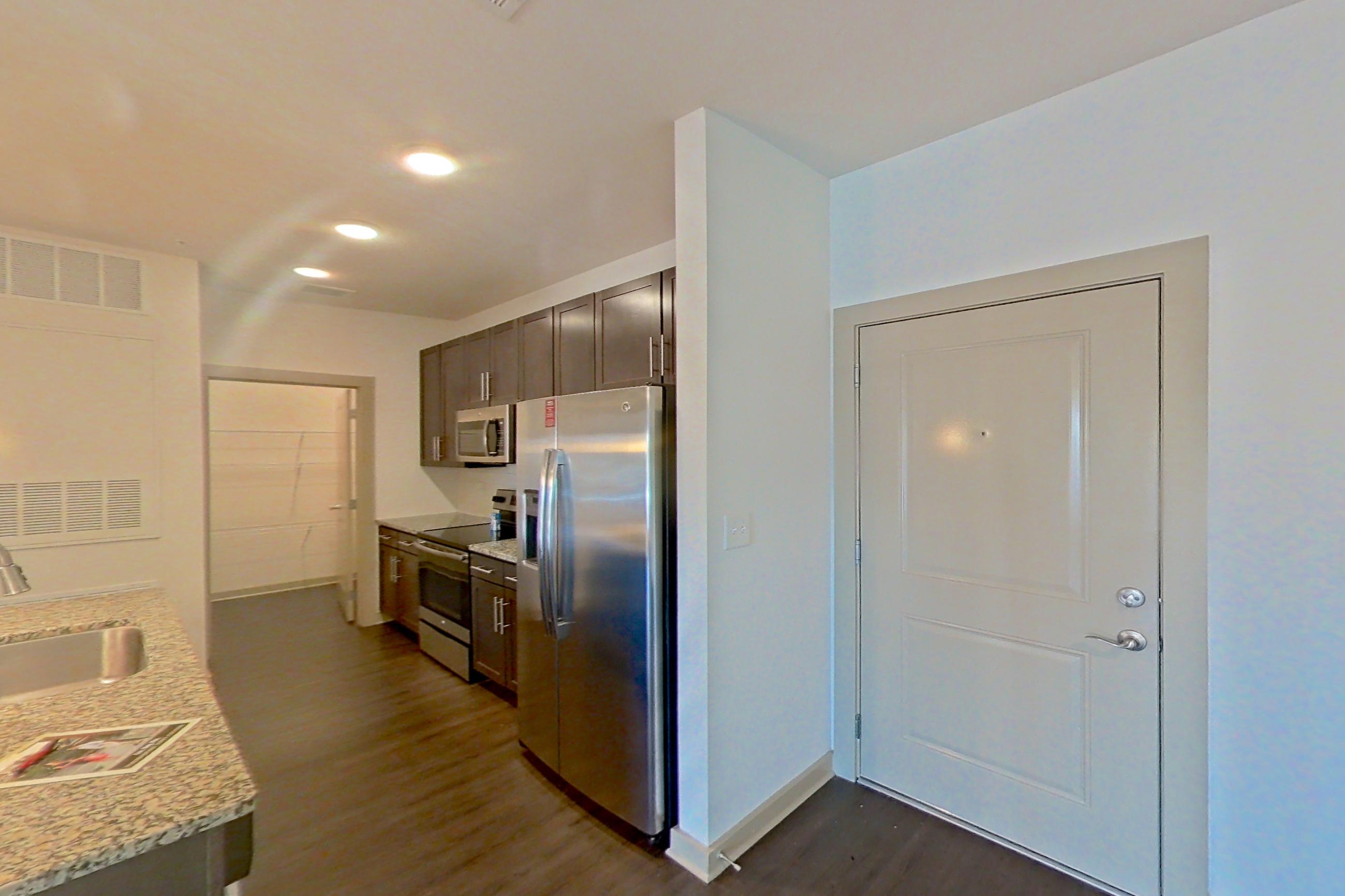 Living room with dark wood-finish flooring, electric range, kitchen island, light stone countertops, oven/range, refrigerator, and stainless steel appliances, Apartment 7-203 at Aventine Northshore