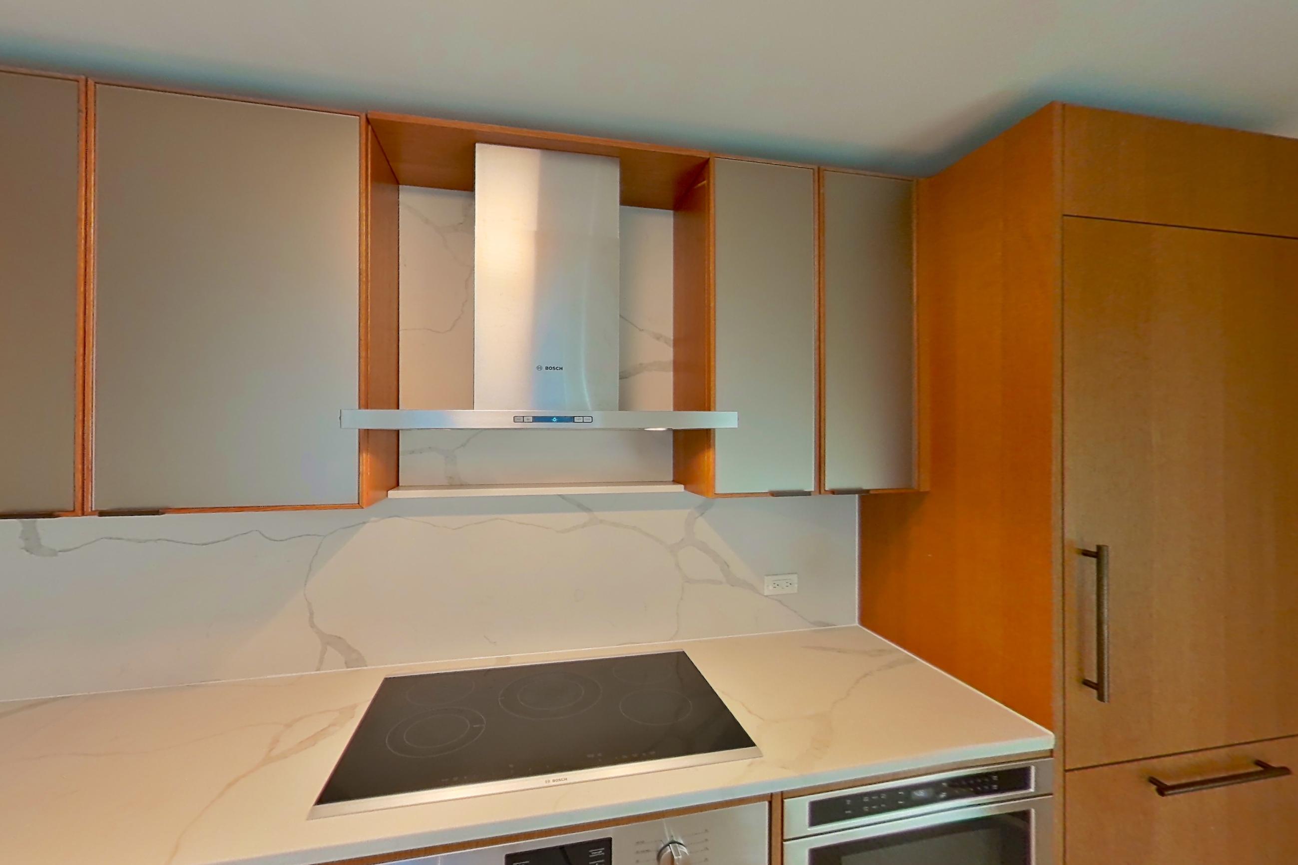 Kitchen with black appliances, cooktop, electric cooktop, light stone countertops, light wood-finish flooring, oven/range, and stainless steel appliances, Apartment 1807 at Oriana