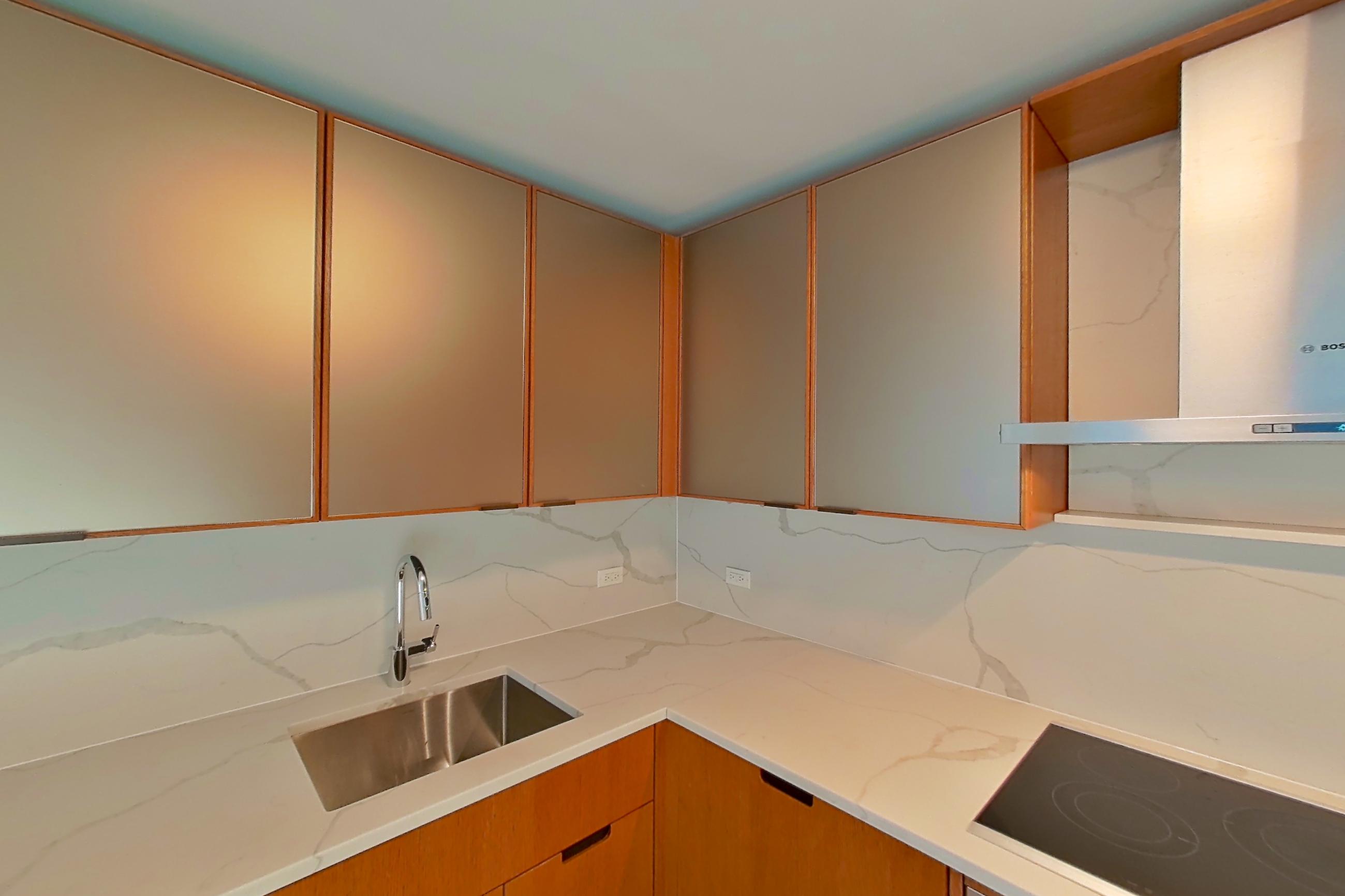 Kitchen with black appliances, cooktop, electric cooktop, light stone countertops, light wood-finish flooring, oven/range, and stainless steel appliances, Apartment 1807 at Oriana