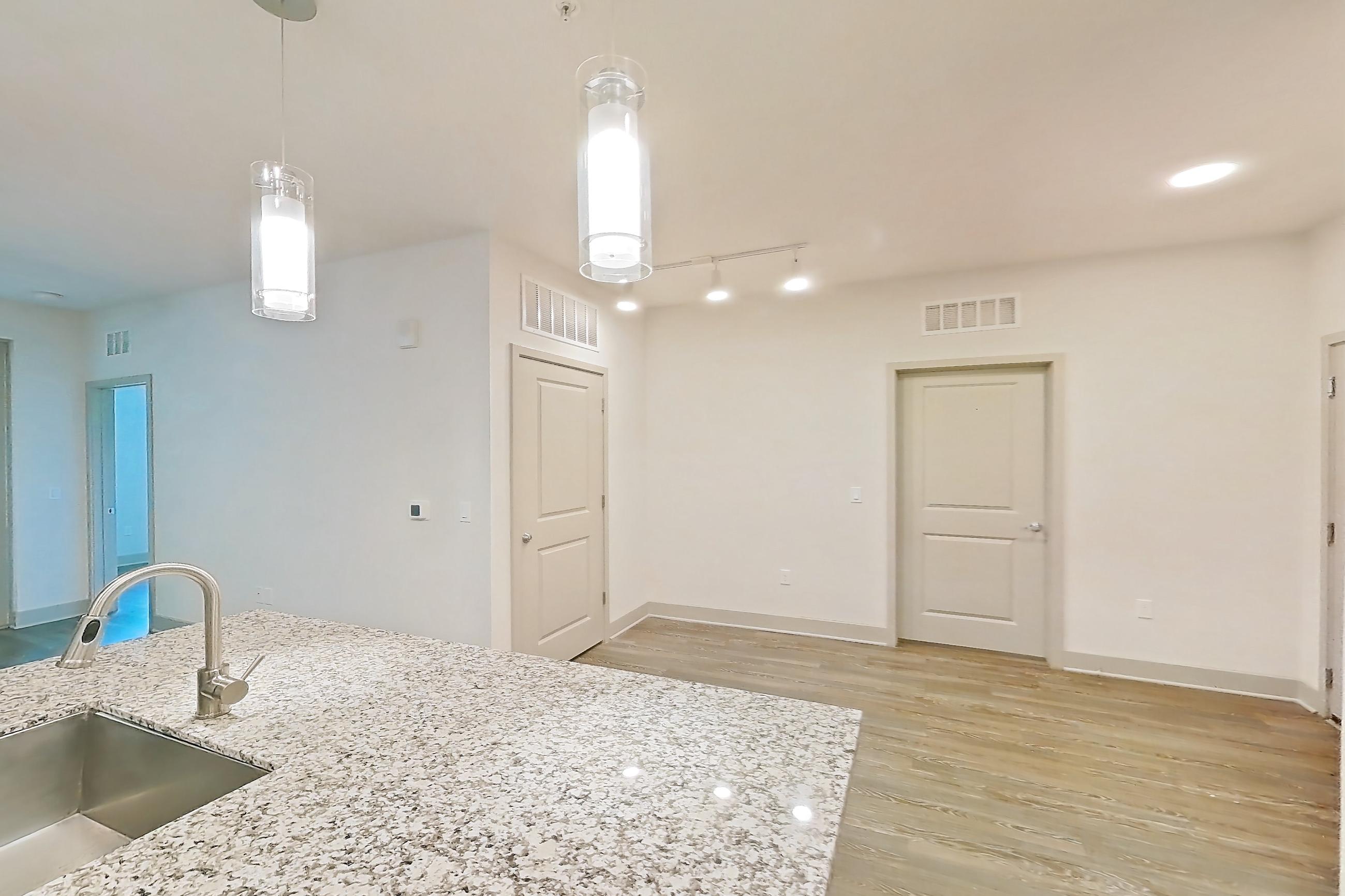 Kitchen with electric range, kitchen island, light countertops, light stone countertops, light wood-finish flooring, microwave, oven/range, refrigerator, stainless steel appliances, and water & ice dispenser, Apartment B3-102 at Lantower Grande Flats
