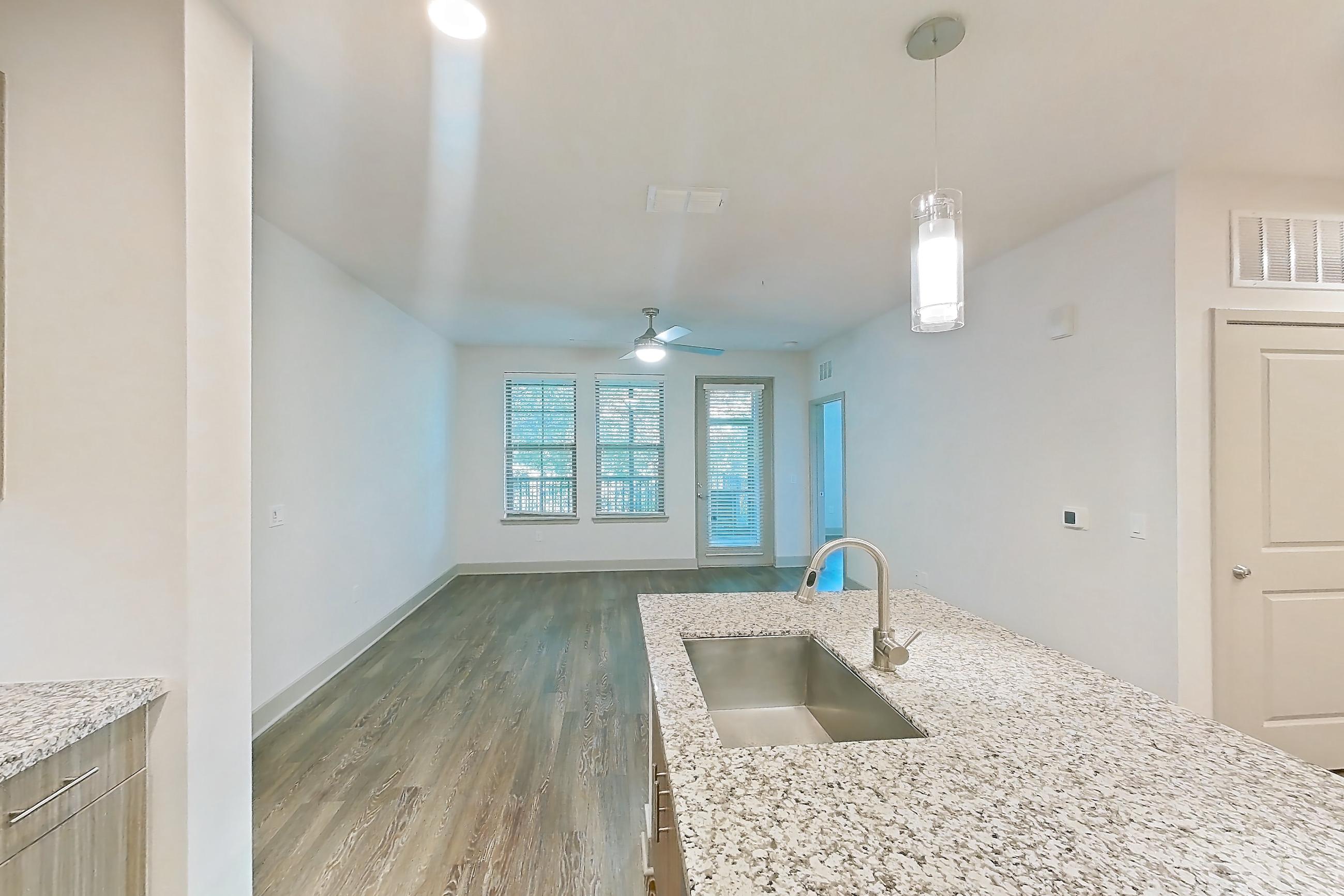 Kitchen with electric range, kitchen island, light countertops, light stone countertops, light wood-finish flooring, microwave, oven/range, refrigerator, stainless steel appliances, and water & ice dispenser, Apartment B3-102 at Lantower Grande Flats