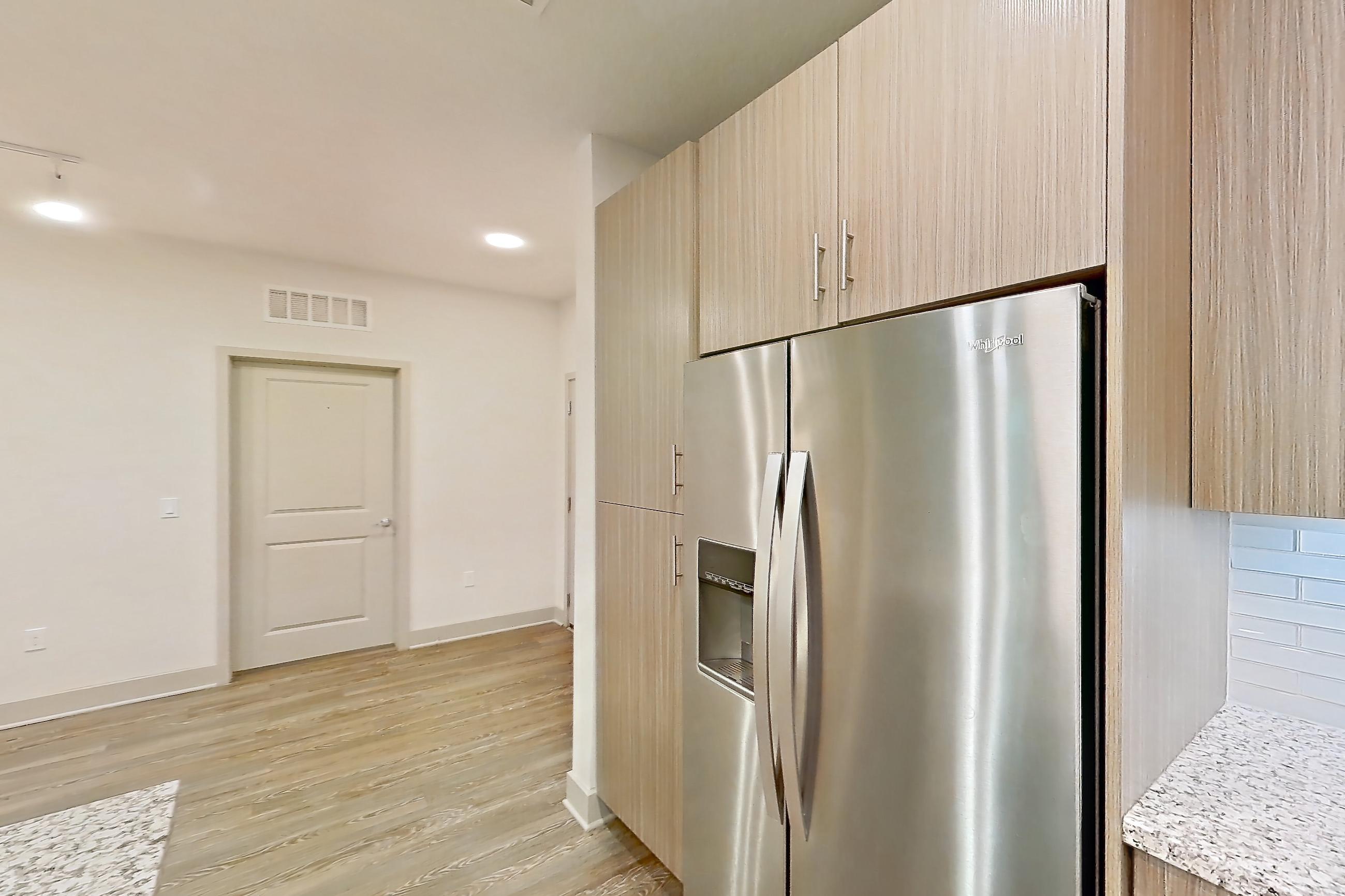 Kitchen with electric range, kitchen island, light countertops, light stone countertops, light wood-finish flooring, microwave, oven/range, refrigerator, stainless steel appliances, and water & ice dispenser, Apartment B3-102 at Lantower Grande Flats
