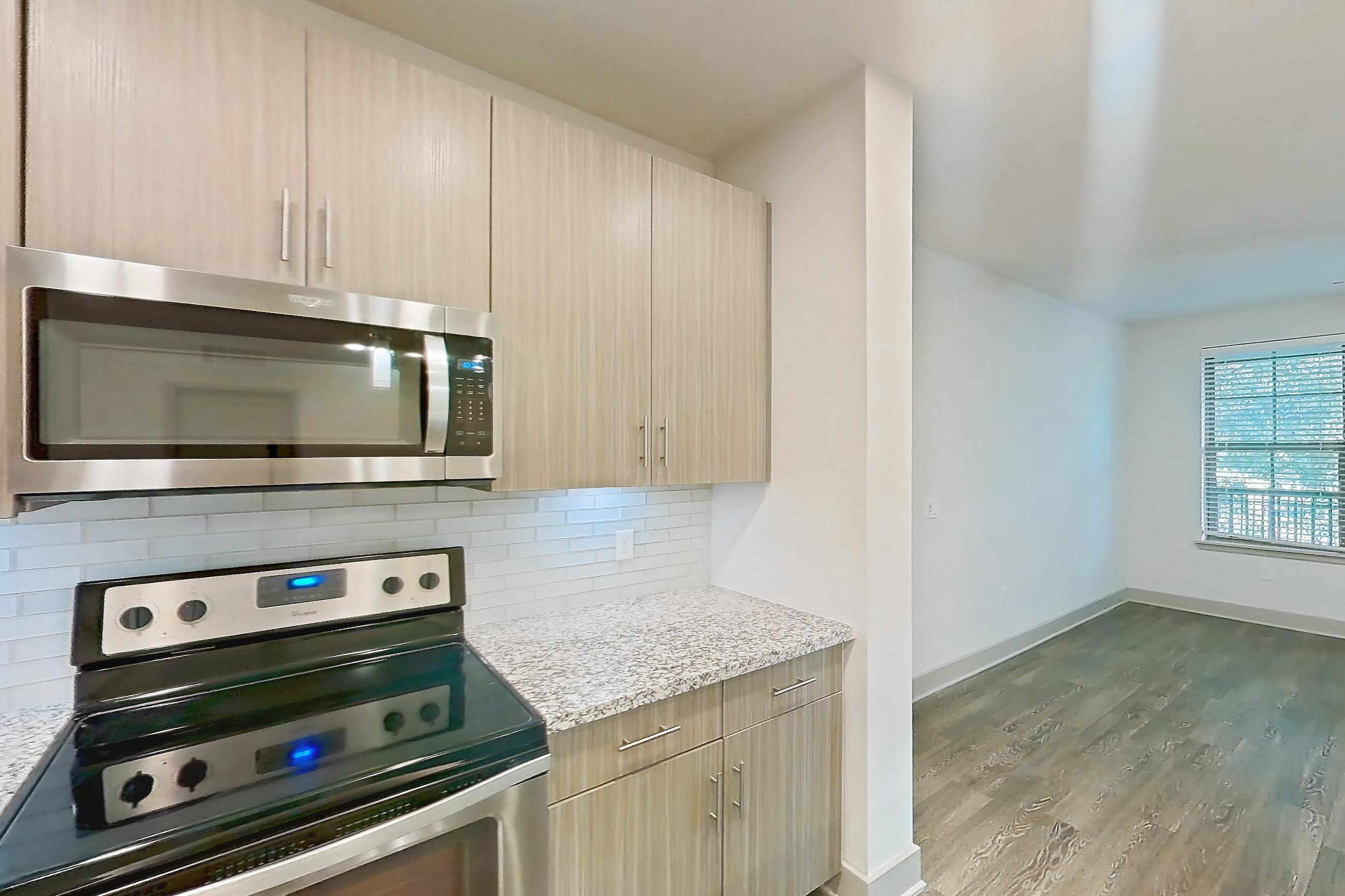 Kitchen with electric range, kitchen island, light countertops, light stone countertops, light wood-finish flooring, microwave, oven/range, refrigerator, stainless steel appliances, and water & ice dispenser, Apartment B3-102 at Lantower Grande Flats