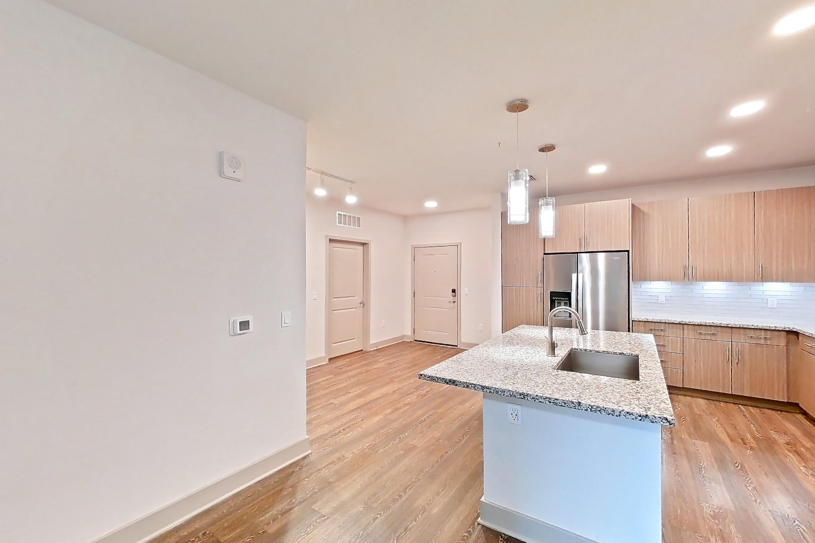 Living room with dark wood-finish flooring, electric range, kitchen island, light stone countertops, light wood-finish flooring, oven/range, refrigerator, stainless steel appliances, and water & ice dispenser, Apartment B3-102 at Lantower Grande Flats