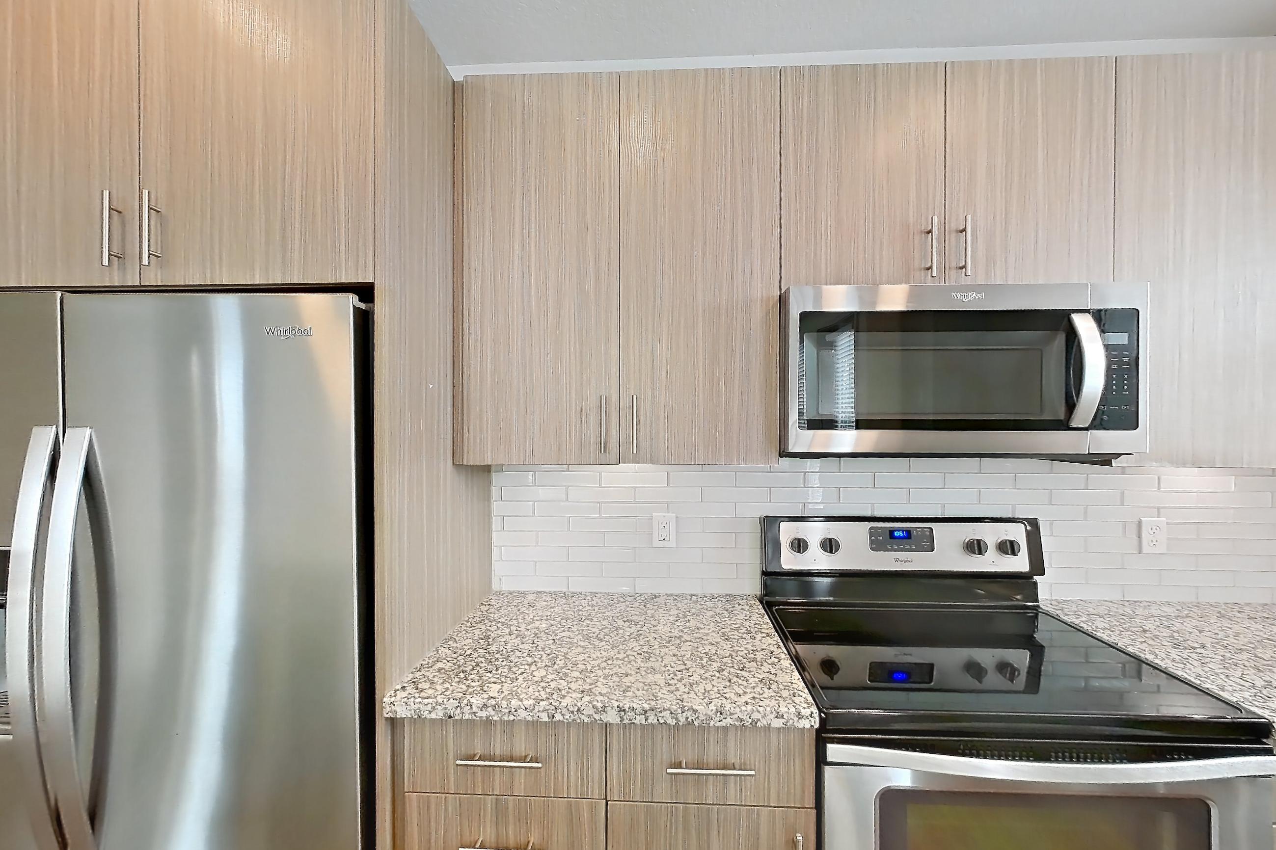 Kitchen with dark wood-finish flooring, dishwasher, electric range, light stone countertops, oven/range, refrigerator, stainless steel appliances, and water & ice dispenser, Apartment B1-201 at Lantower Grande Flats
