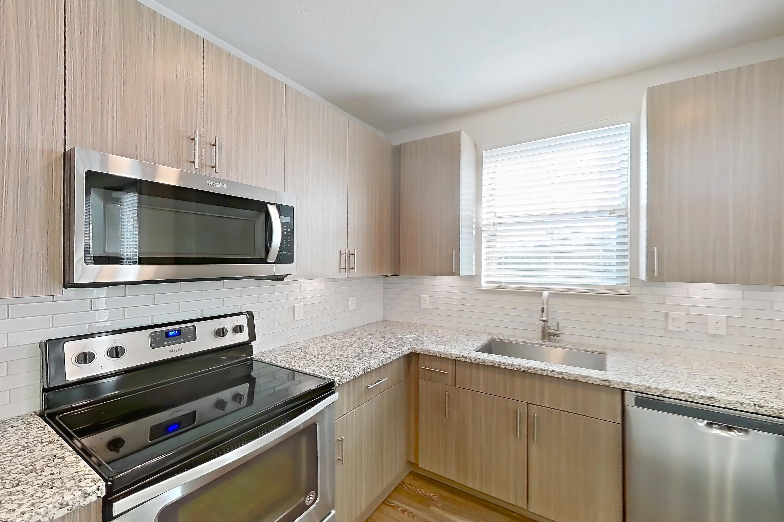Kitchen with dark wood-finish flooring, dishwasher, electric range, light stone countertops, oven/range, refrigerator, stainless steel appliances, and water & ice dispenser, Apartment B1-201 at Lantower Grande Flats