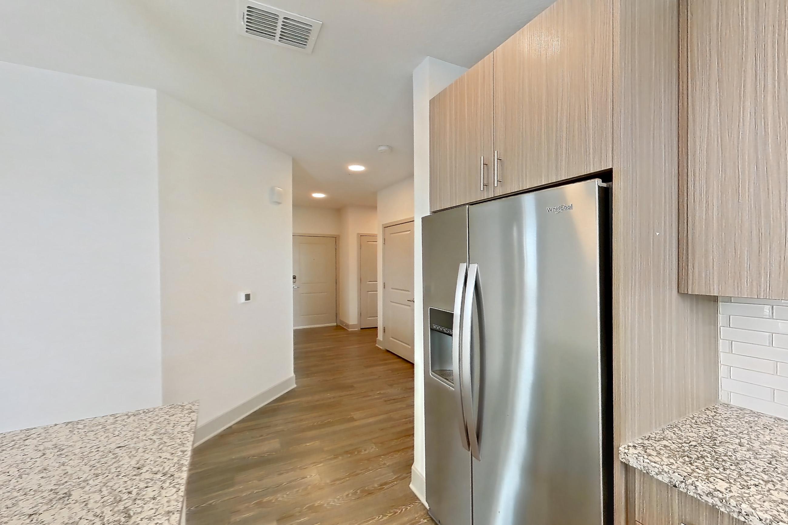 Kitchen with dark wood-finish flooring, dishwasher, electric range, light stone countertops, oven/range, refrigerator, stainless steel appliances, and water & ice dispenser, Apartment B1-201 at Lantower Grande Flats