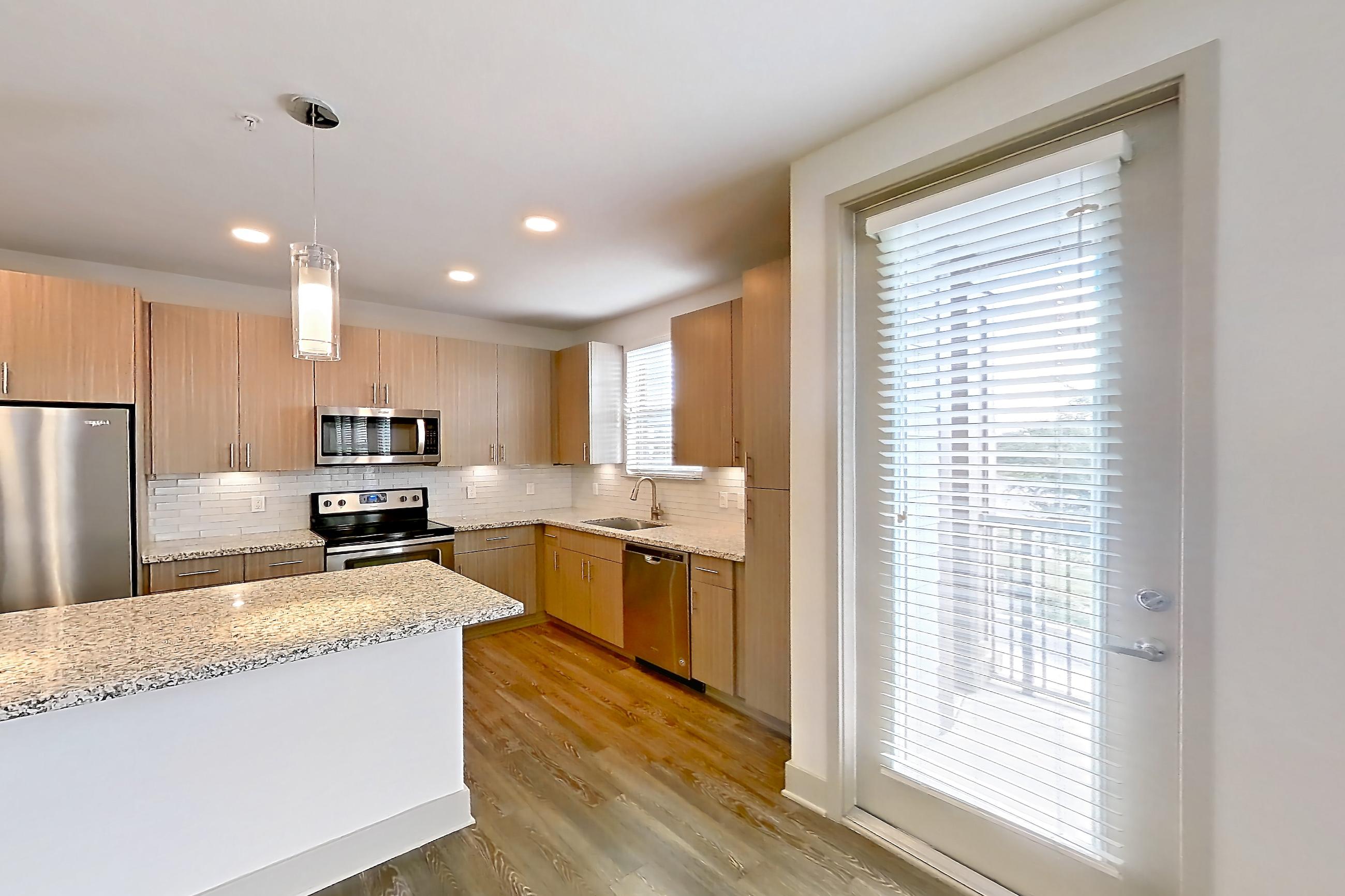 Living room with dark wood-finish flooring, dishwasher, electric range, light stone countertops, oven/range, refrigerator, stainless steel appliances, and water & ice dispenser, Apartment B1-201 at Lantower Grande Flats
