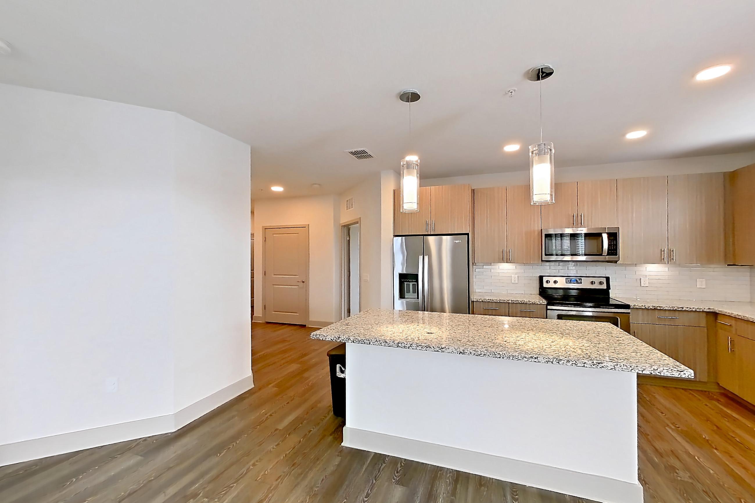 Living room with dark wood-finish flooring, dishwasher, electric range, light stone countertops, oven/range, refrigerator, stainless steel appliances, and water & ice dispenser, Apartment B1-201 at Lantower Grande Flats