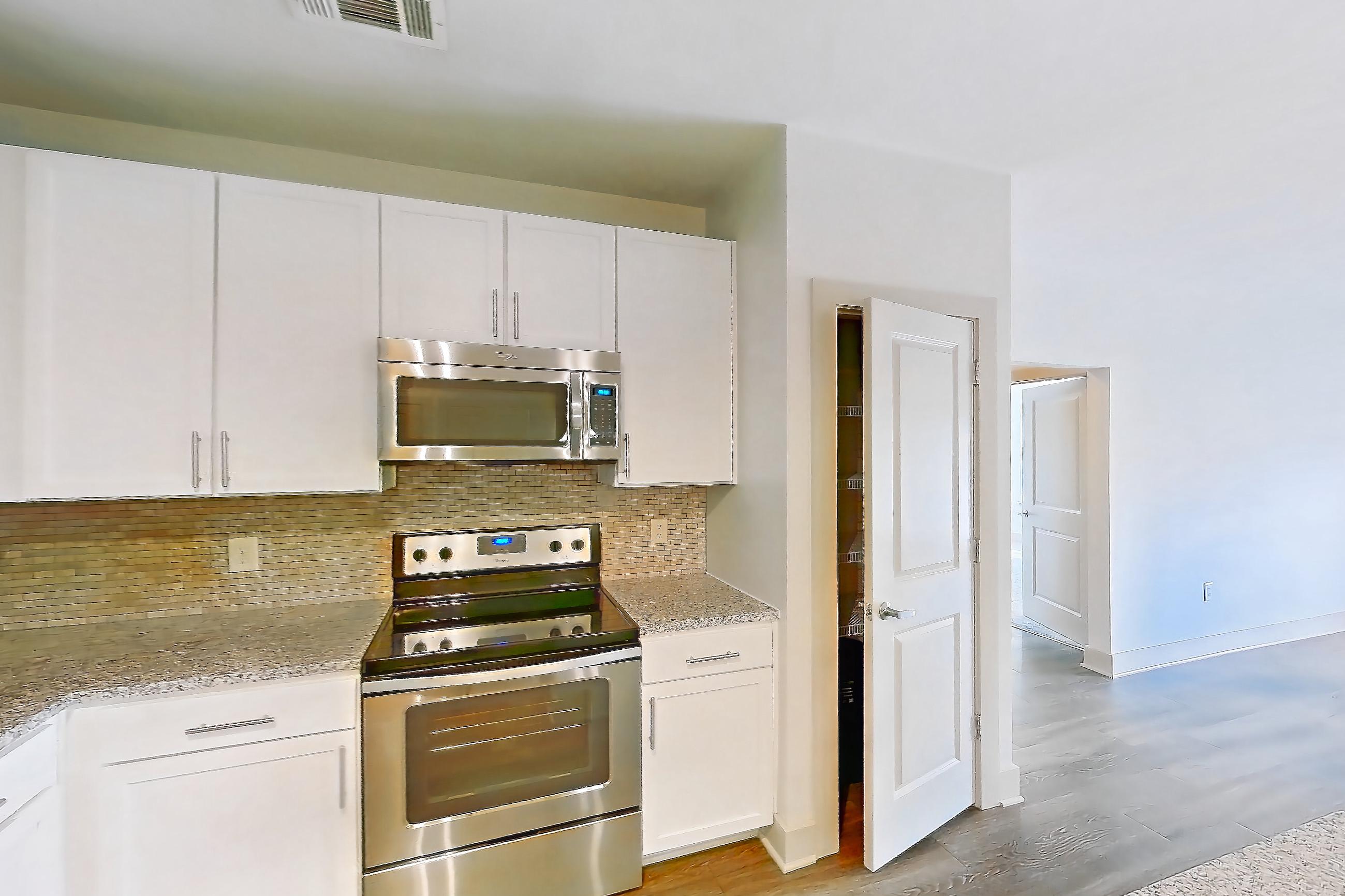 Kitchen with dark wood-finish flooring, dishwasher, electric range, light countertops, light stone countertops, light wood-finish flooring, microwave, oven/range, and stainless steel appliances, Apartment 1208 at Lantower Waverly