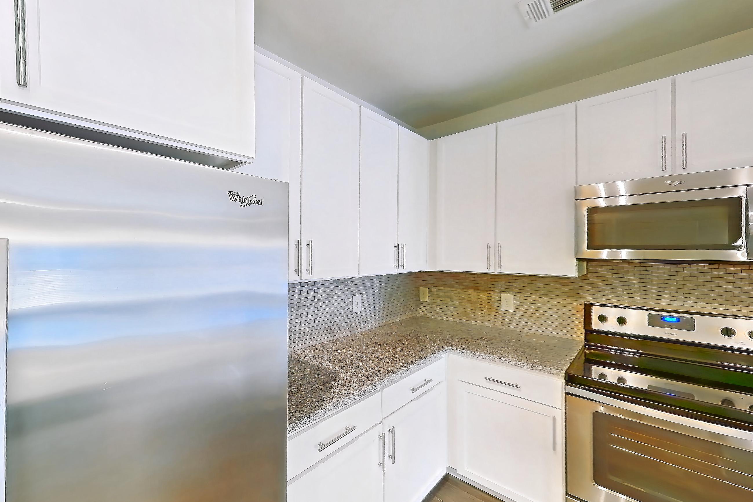 Kitchen with dark wood-finish flooring, dishwasher, electric range, light countertops, light stone countertops, light wood-finish flooring, microwave, oven/range, and stainless steel appliances, Apartment 1208 at Lantower Waverly