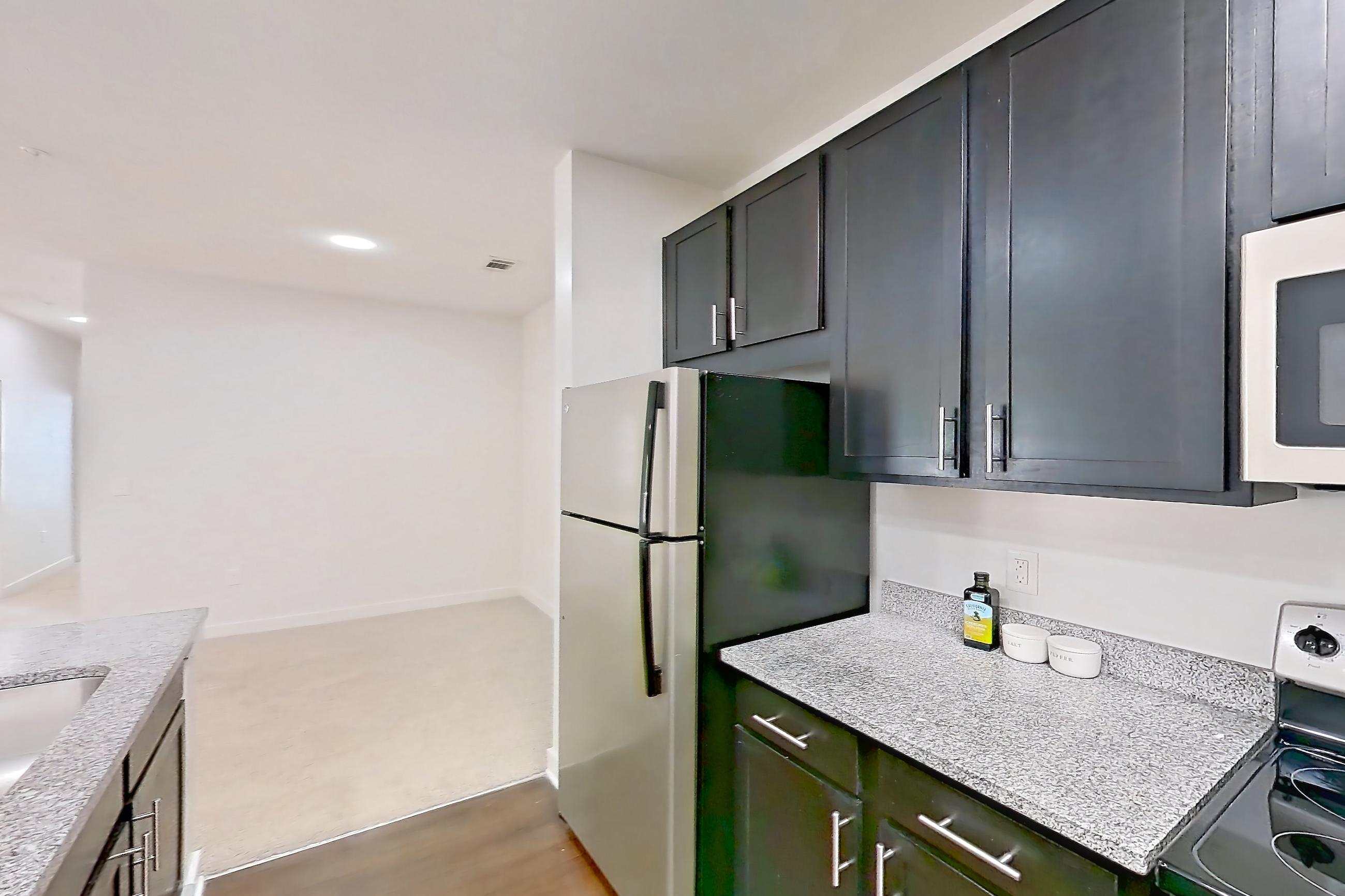 Kitchen with black appliances, dark wood-finish flooring, electric range, light countertops, light stone countertops, light wood-finish flooring, microwave, oven/range, refrigerator, and stainless steel appliances, Apartment 208 at Realm at Patterson Place