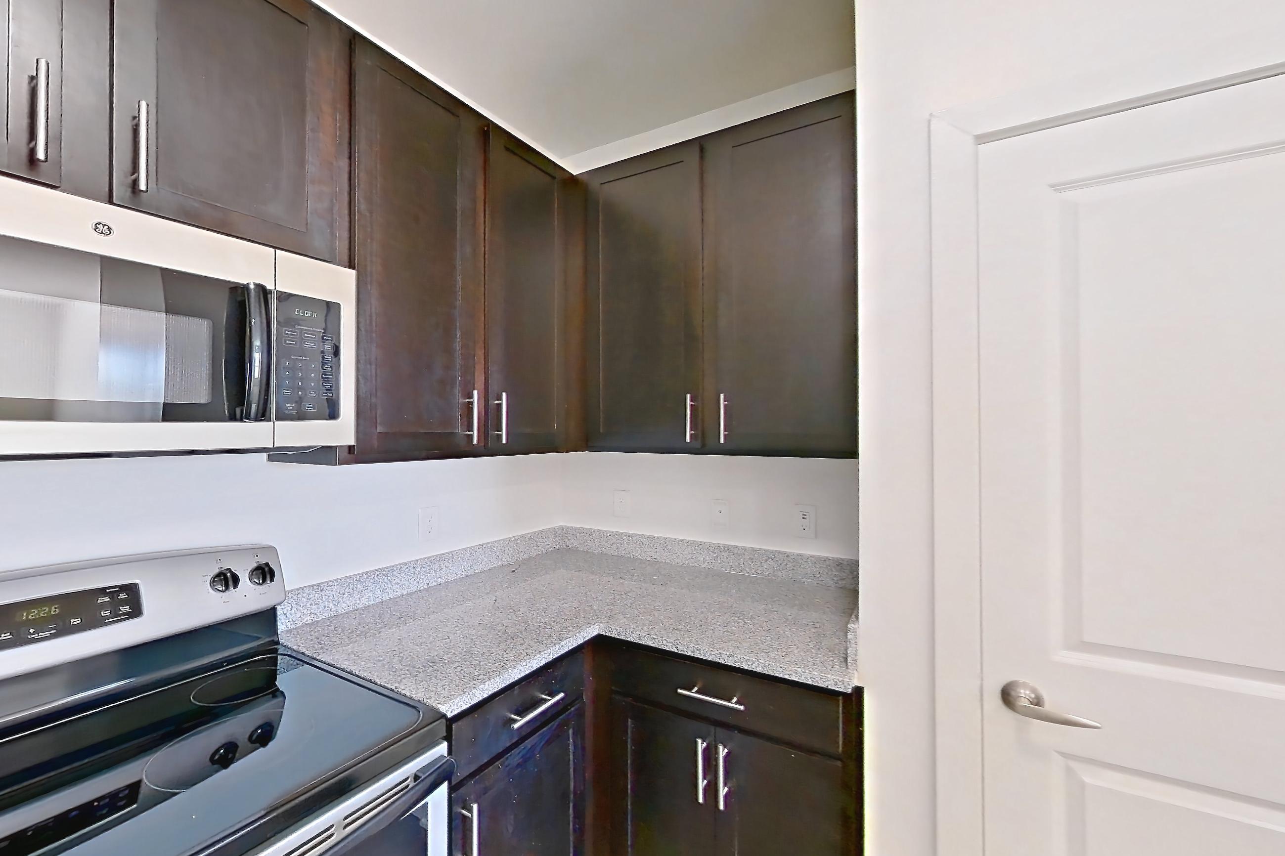 Kitchen with dark wood-finish flooring, dishwasher, electric range, light countertops, light stone countertops, light wood-finish flooring, microwave, oven/range, refrigerator, and stainless steel appliances, Apartment 101 at Realm at Patterson Place