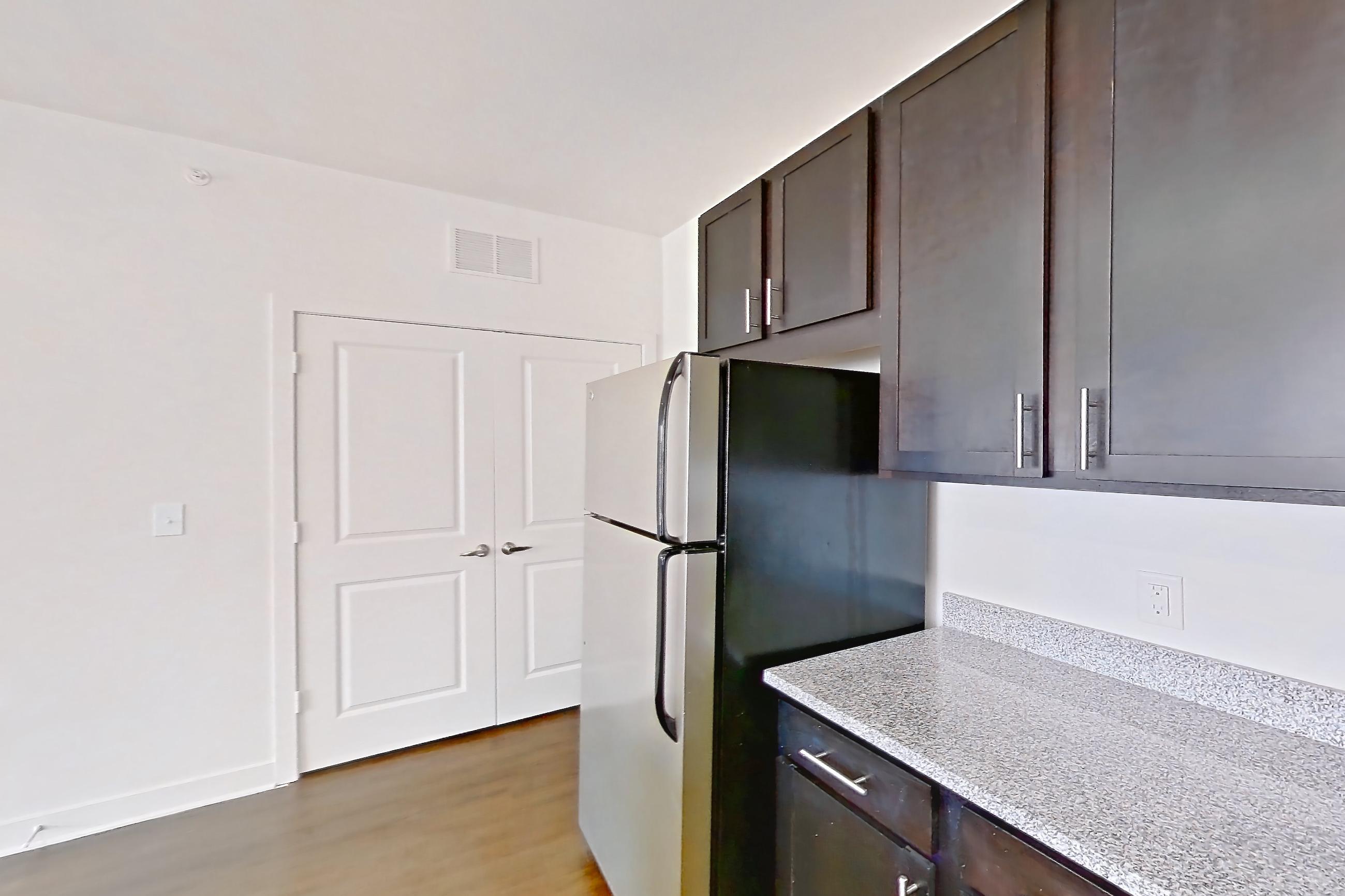 Kitchen with dark wood-finish flooring, dishwasher, electric range, light countertops, light stone countertops, light wood-finish flooring, microwave, oven/range, refrigerator, and stainless steel appliances, Apartment 101 at Realm at Patterson Place