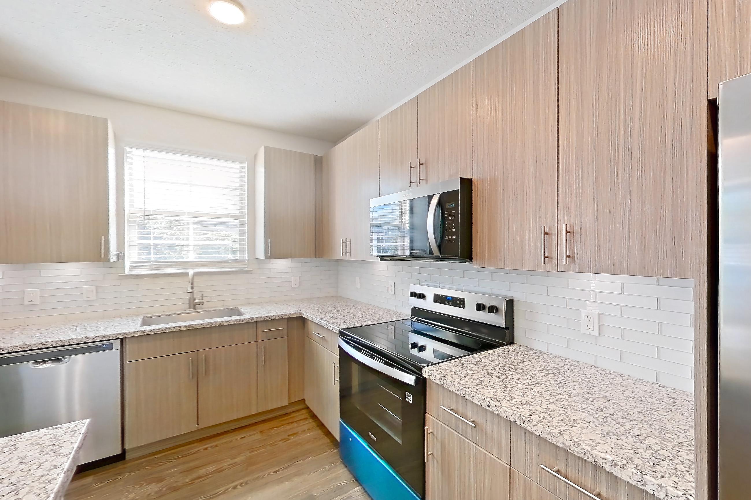 Kitchen with dark wood-finish flooring, dishwasher, electric range, light countertops, light stone countertops, oven/range, and stainless steel appliances, Apartment B2-102 at Lantower Grande Flats
