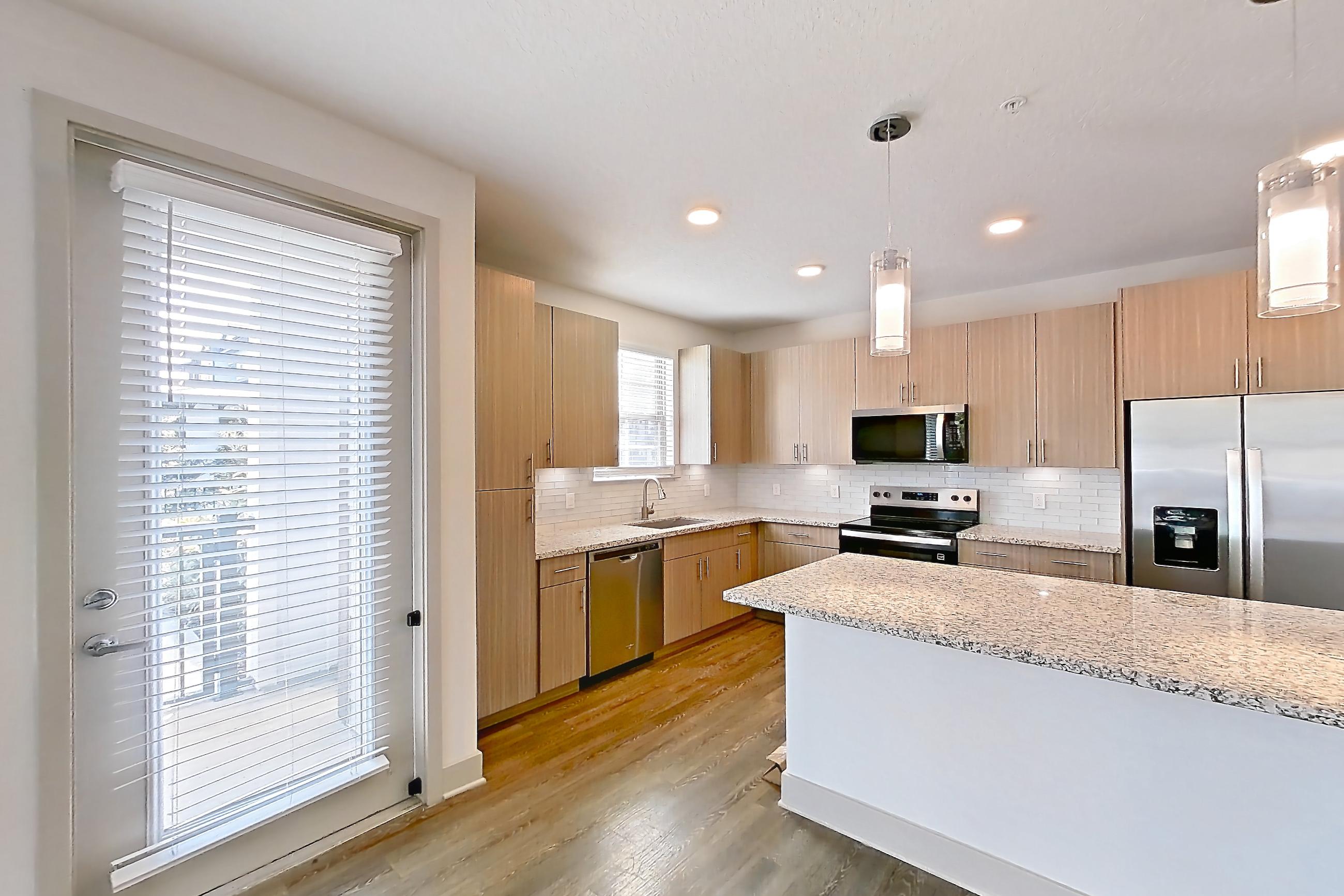 Living room with dark wood-finish flooring, dishwasher, electric range, light stone countertops, oven/range, refrigerator, stainless steel appliances, and water & ice dispenser, Apartment B2-102 at Lantower Grande Flats