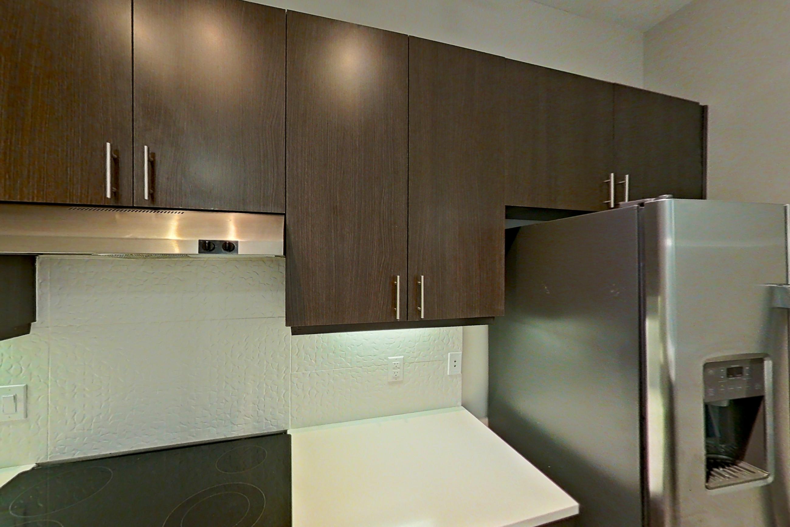 Kitchen with dishwasher, electric range, light countertops, light wood-finish flooring, microwave, oven/range, range hood, refrigerator, stainless steel appliances, and water & ice dispenser, Apartment 331 at BullHouse