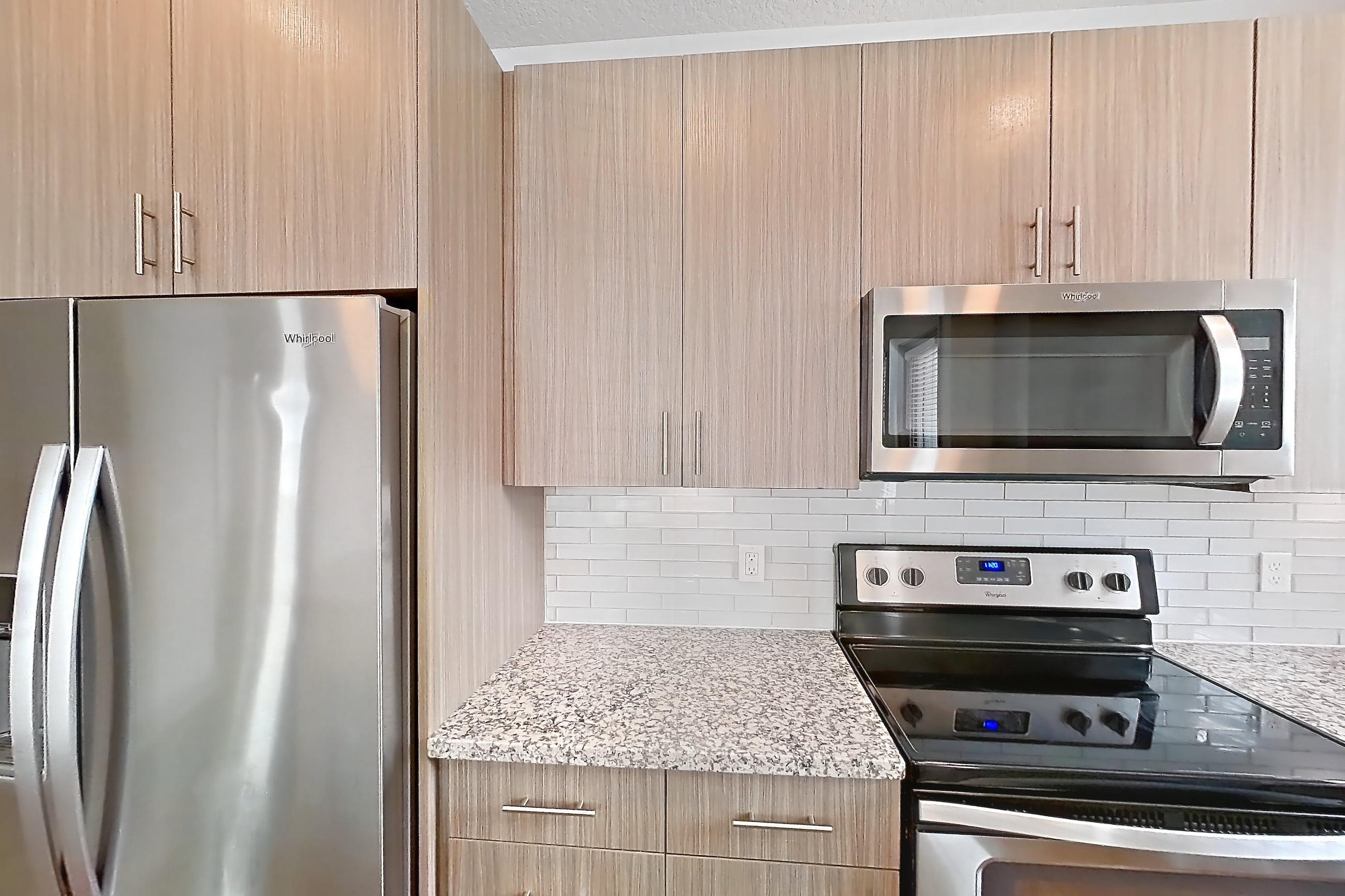 Kitchen with dark wood-finish flooring, dishwasher, electric range, light stone countertops, oven/range, refrigerator, and stainless steel appliances, Apartment B2-112 at Lantower Grande Flats