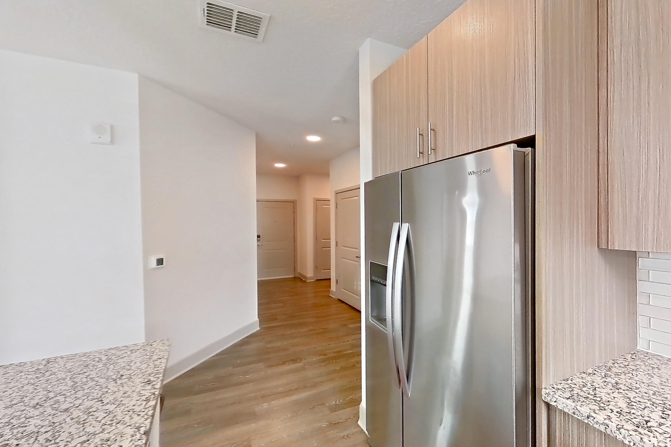 Kitchen with dark wood-finish flooring, dishwasher, electric range, light stone countertops, oven/range, refrigerator, and stainless steel appliances, Apartment B2-112 at Lantower Grande Flats