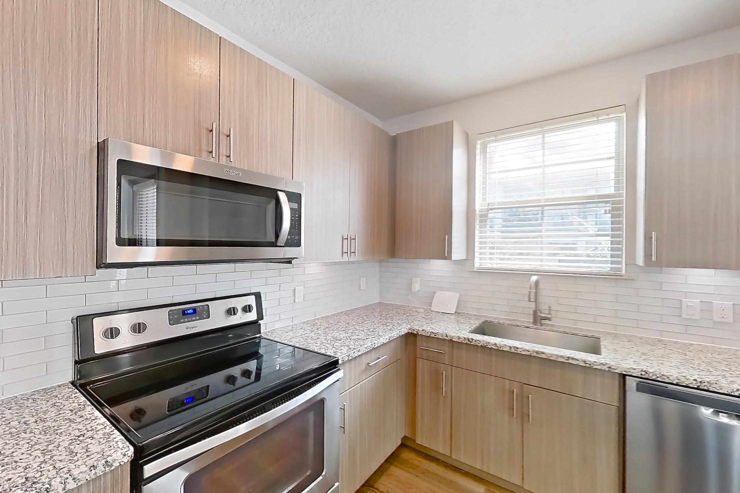 Kitchen with dark wood-finish flooring, dishwasher, electric range, light stone countertops, oven/range, refrigerator, and stainless steel appliances, Apartment B2-112 at Lantower Grande Flats