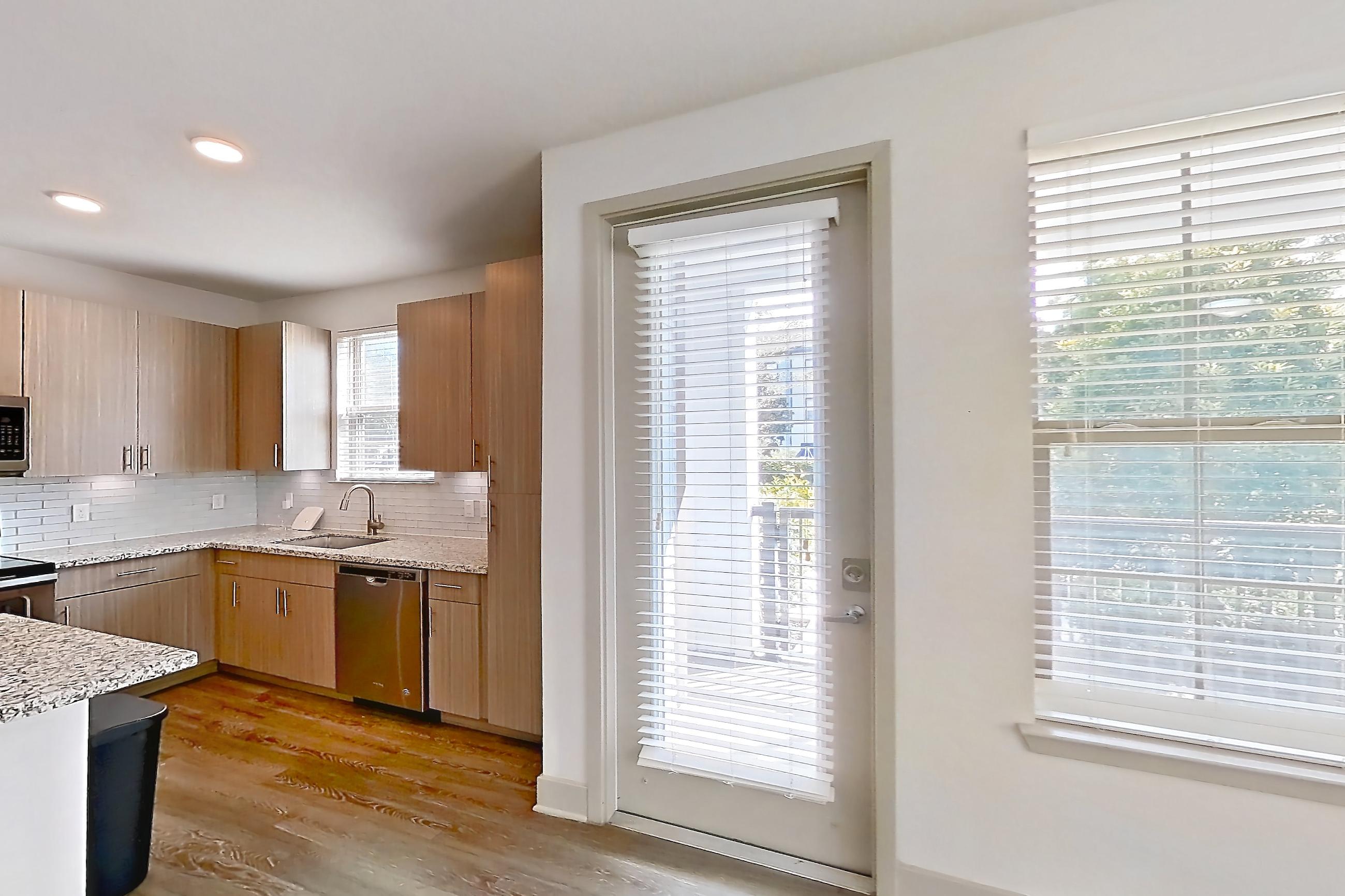 Living room with dark wood-finish flooring, dishwasher, electric range, light stone countertops, oven/range, refrigerator, stainless steel appliances, and water & ice dispenser, Apartment B2-112 at Lantower Grande Flats