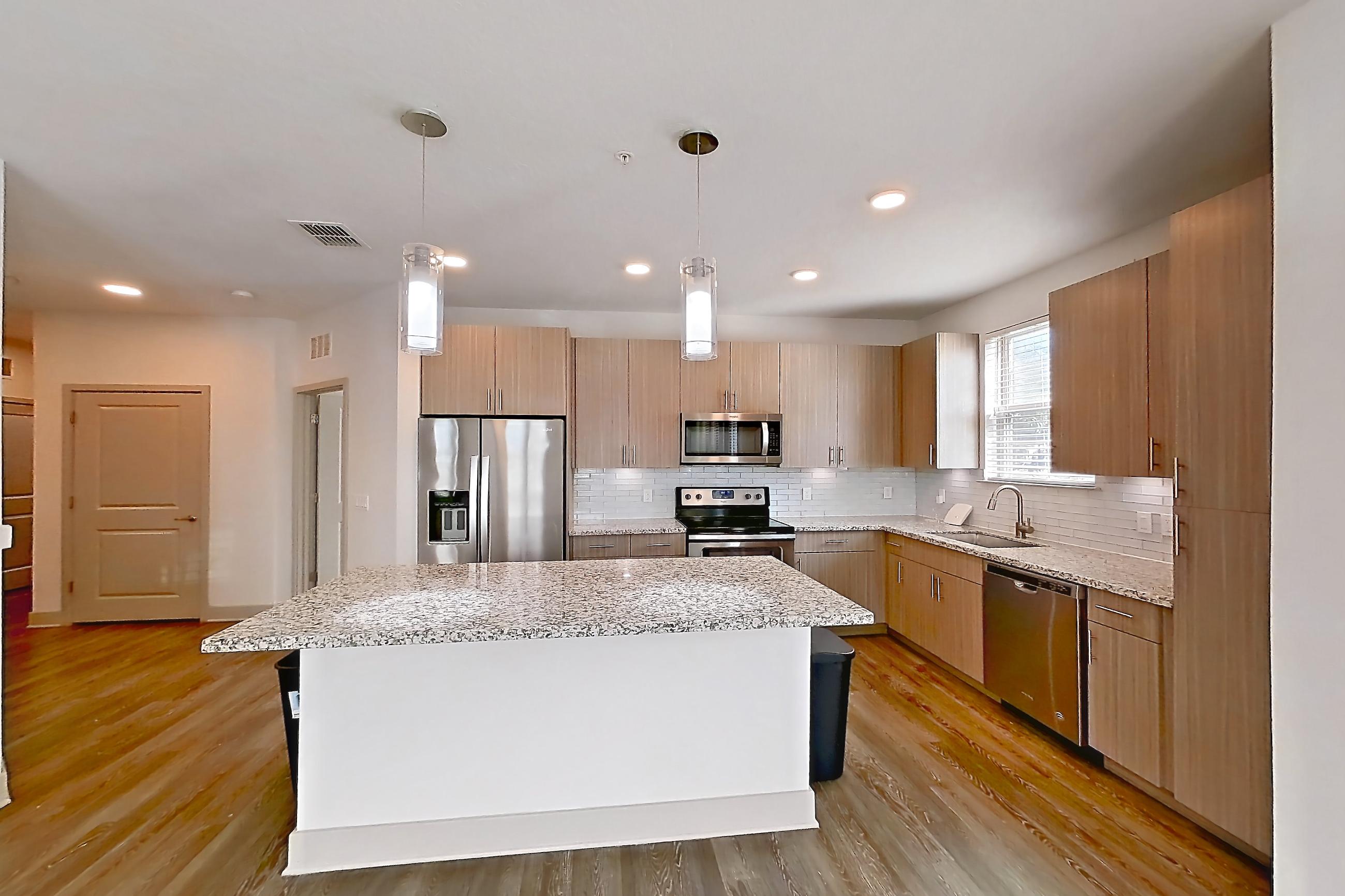 Living room with dark wood-finish flooring, dishwasher, electric range, light stone countertops, oven/range, refrigerator, stainless steel appliances, and water & ice dispenser, Apartment B2-112 at Lantower Grande Flats