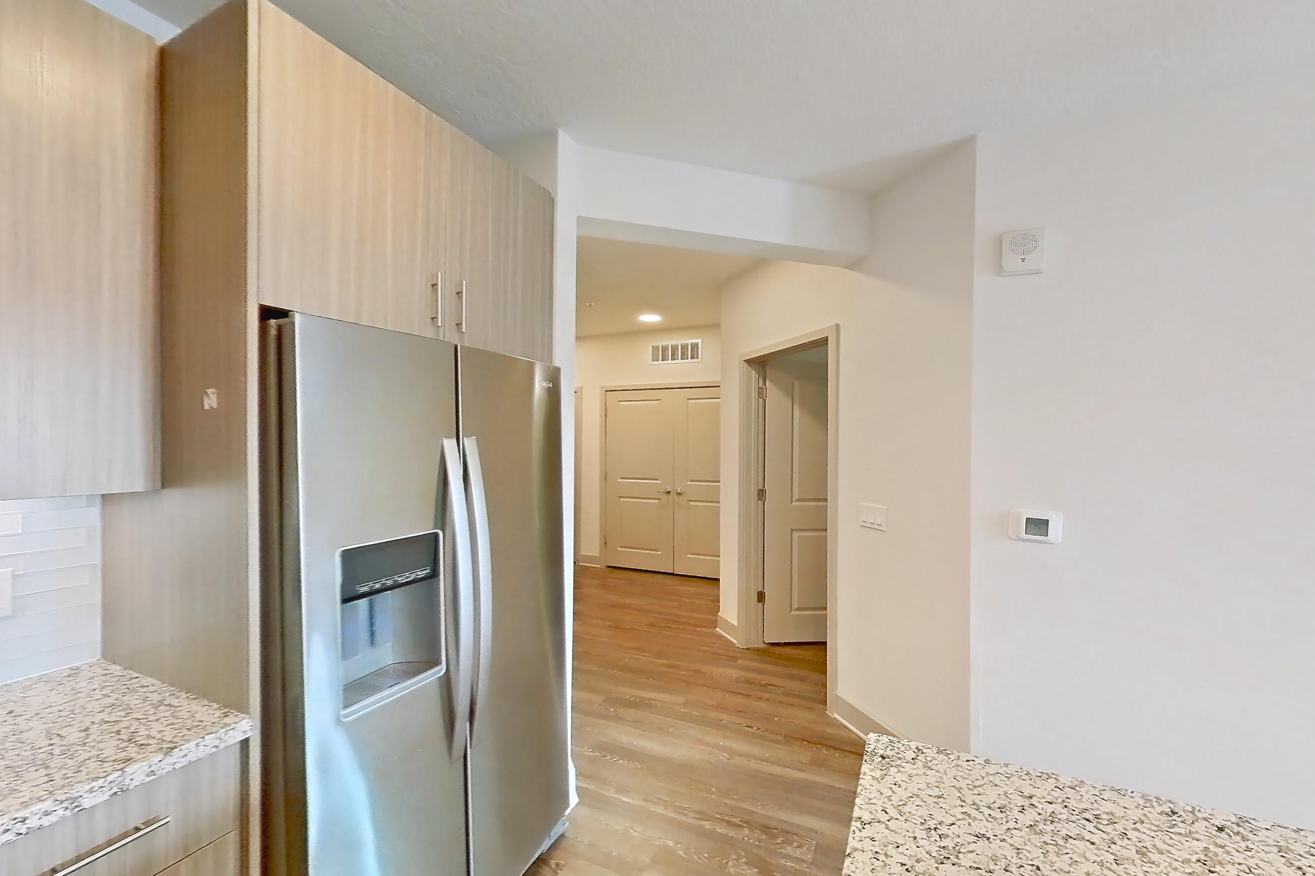 Kitchen with dark wood-finish flooring, dishwasher, electric range, light countertops, light stone countertops, light wood-finish flooring, microwave, oven/range, refrigerator, stainless steel appliances, and water & ice dispenser, Apartment B2-304 at Lantower Grande Flats