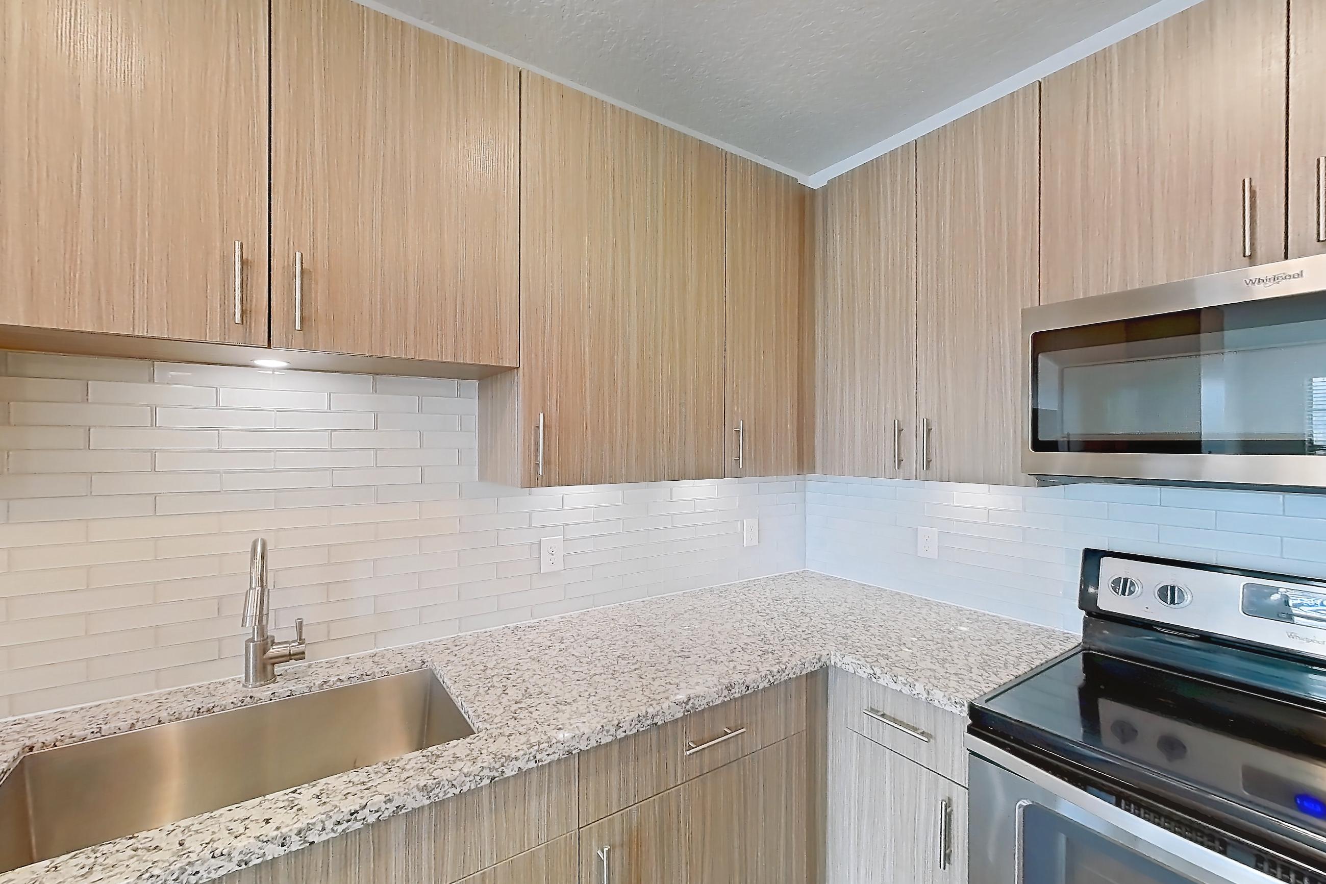 Kitchen with dark wood-finish flooring, dishwasher, electric range, light countertops, light stone countertops, light wood-finish flooring, microwave, oven/range, refrigerator, stainless steel appliances, and water & ice dispenser, Apartment B2-304 at Lantower Grande Flats