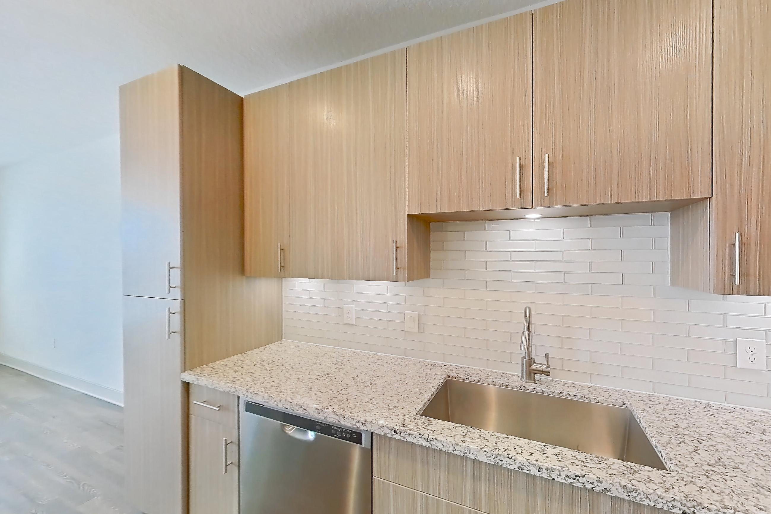 Kitchen with dark wood-finish flooring, dishwasher, electric range, light countertops, light stone countertops, light wood-finish flooring, microwave, oven/range, refrigerator, stainless steel appliances, and water & ice dispenser, Apartment B2-304 at Lantower Grande Flats