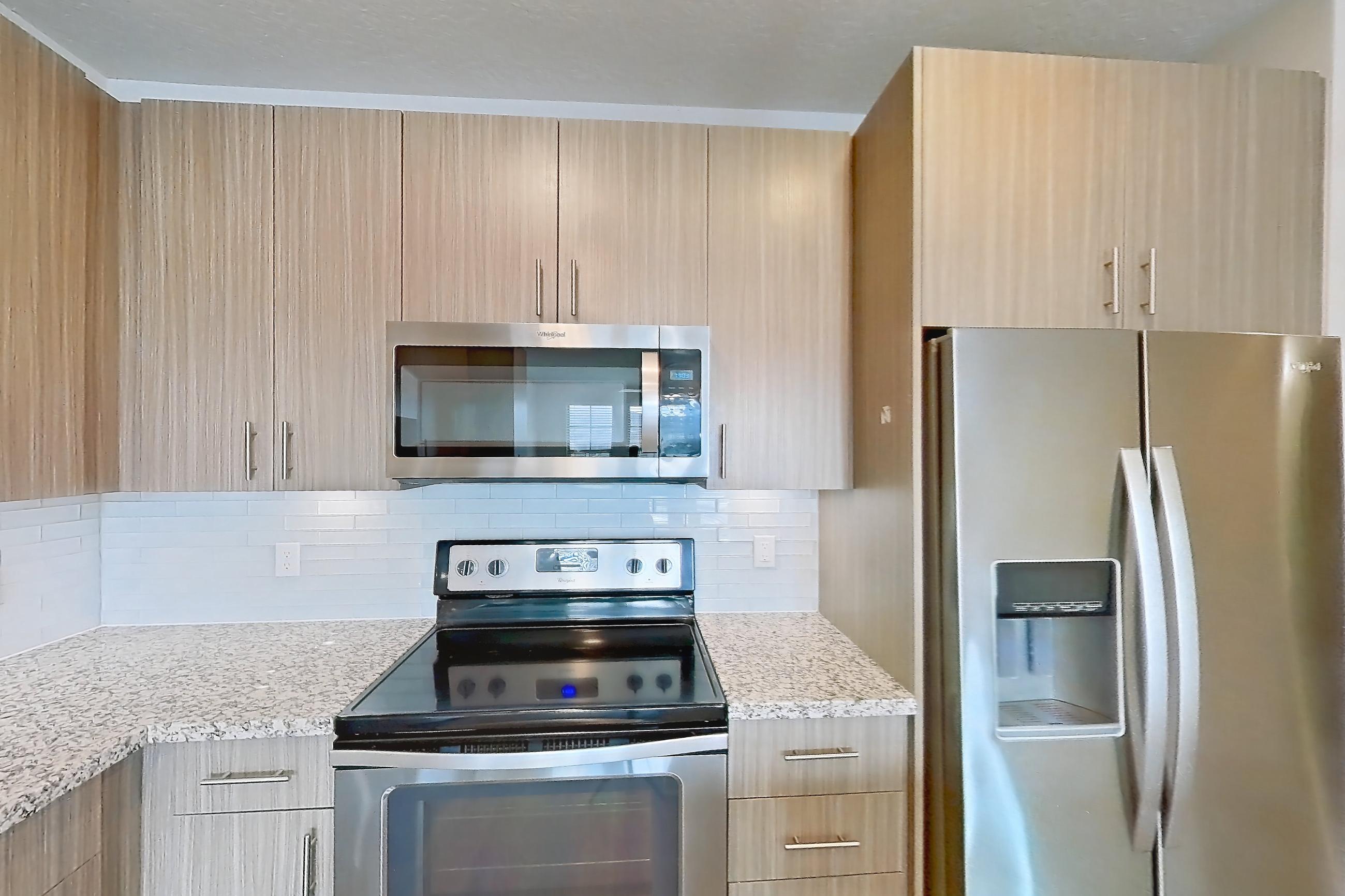 Kitchen with dark wood-finish flooring, dishwasher, electric range, light countertops, light stone countertops, light wood-finish flooring, microwave, oven/range, refrigerator, stainless steel appliances, and water & ice dispenser, Apartment B2-304 at Lantower Grande Flats