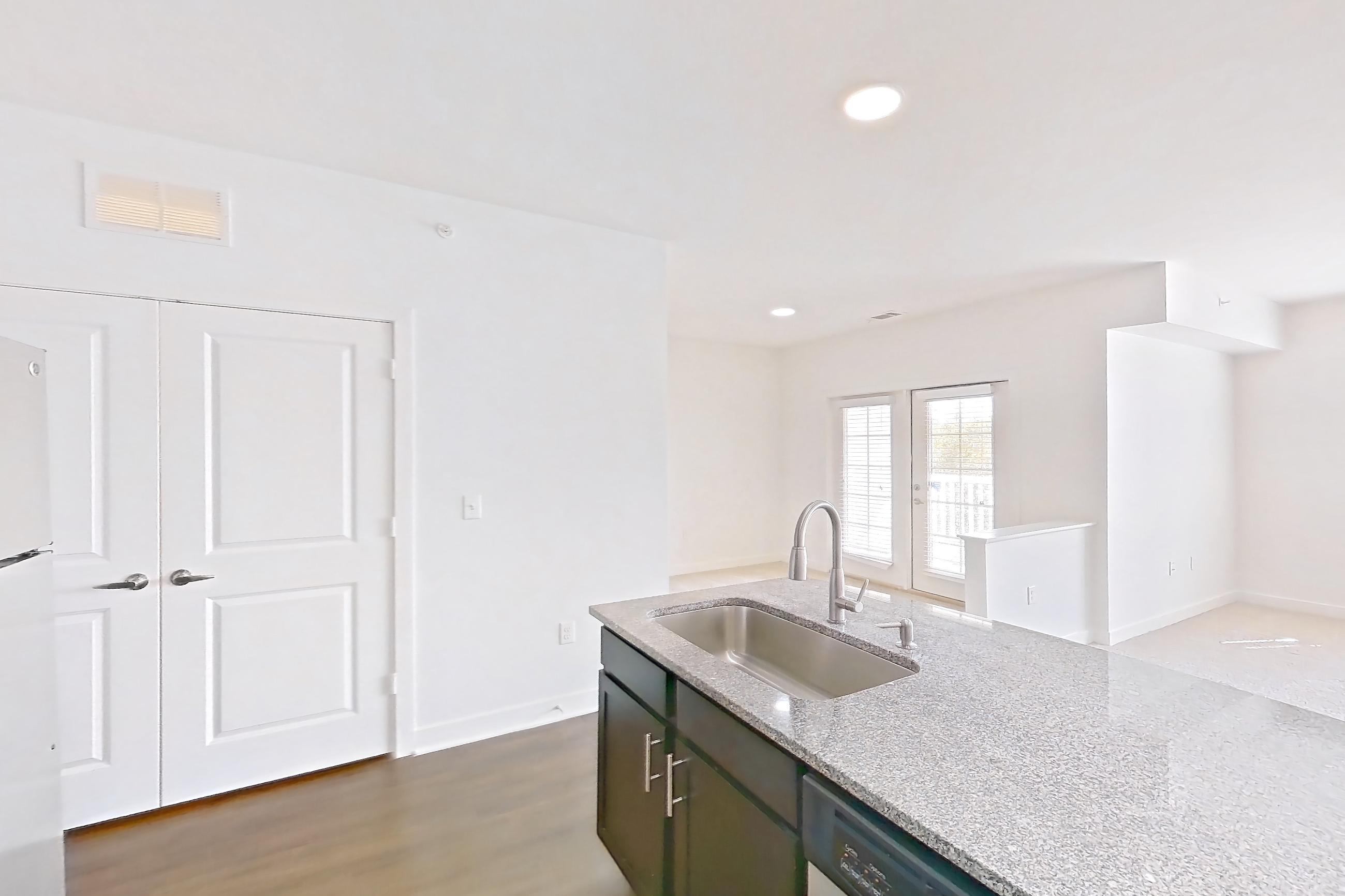 Kitchen with dark wood-finish flooring, dishwasher, electric range, light countertops, light stone countertops, light wood-finish flooring, microwave, oven/range, refrigerator, and stainless steel appliances, Apartment 306 at Realm at Patterson Place