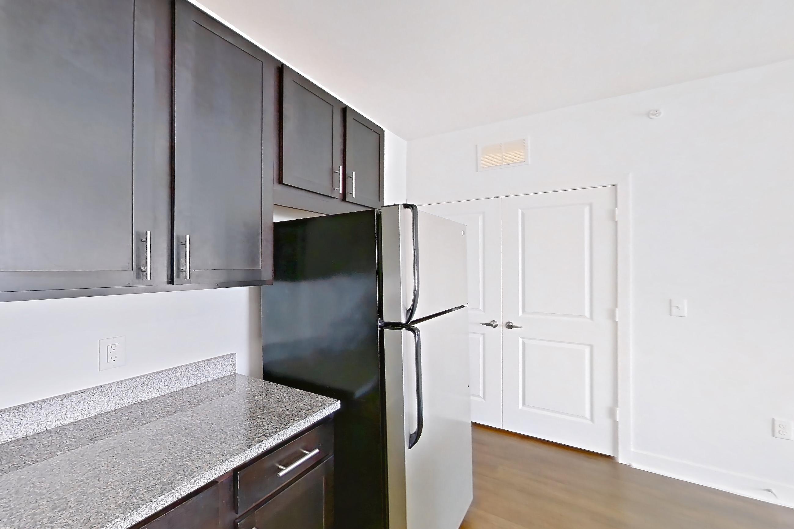 Kitchen with dark wood-finish flooring, dishwasher, electric range, light countertops, light stone countertops, light wood-finish flooring, microwave, oven/range, refrigerator, and stainless steel appliances, Apartment 306 at Realm at Patterson Place