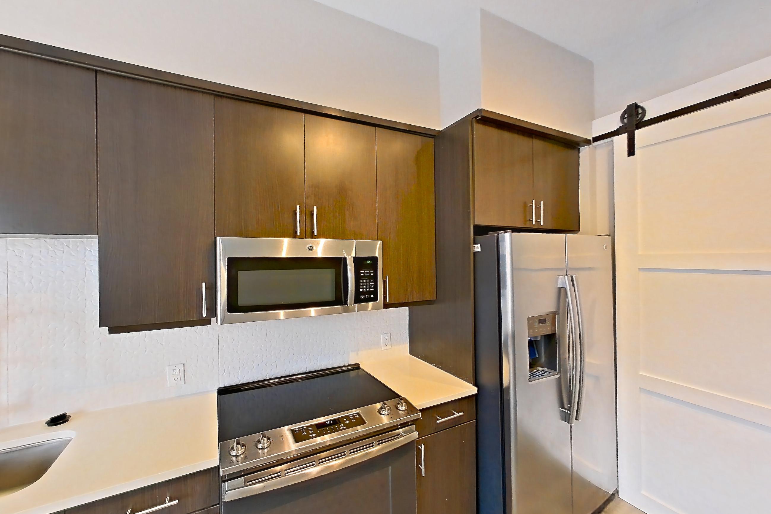 Kitchen with dishwasher, electric range, light countertops, light wood-finish flooring, microwave, oven/range, refrigerator, stainless steel appliances, and water & ice dispenser, Apartment 415 at BullHouse