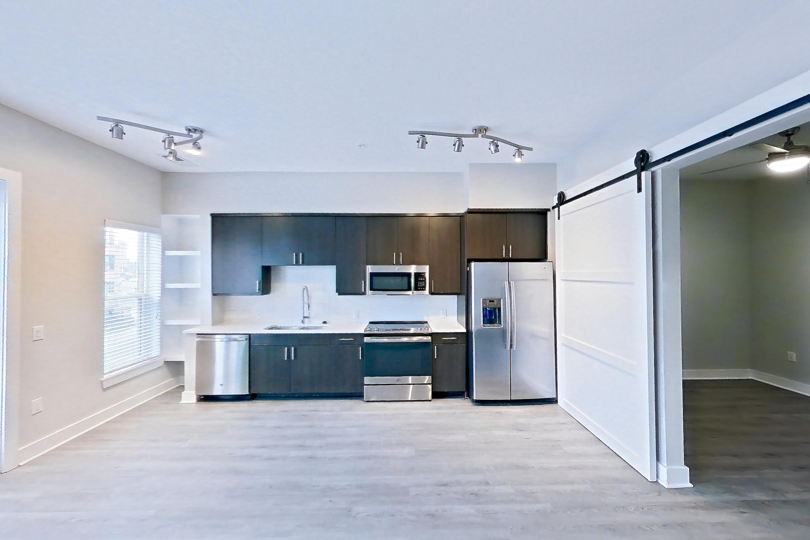 Living room with dark wood-finish flooring, dishwasher, electric range, light countertops, light vinyl flooring, light wood-finish flooring, microwave, oven/range, refrigerator, and stainless steel appliances, Apartment 415 at BullHouse