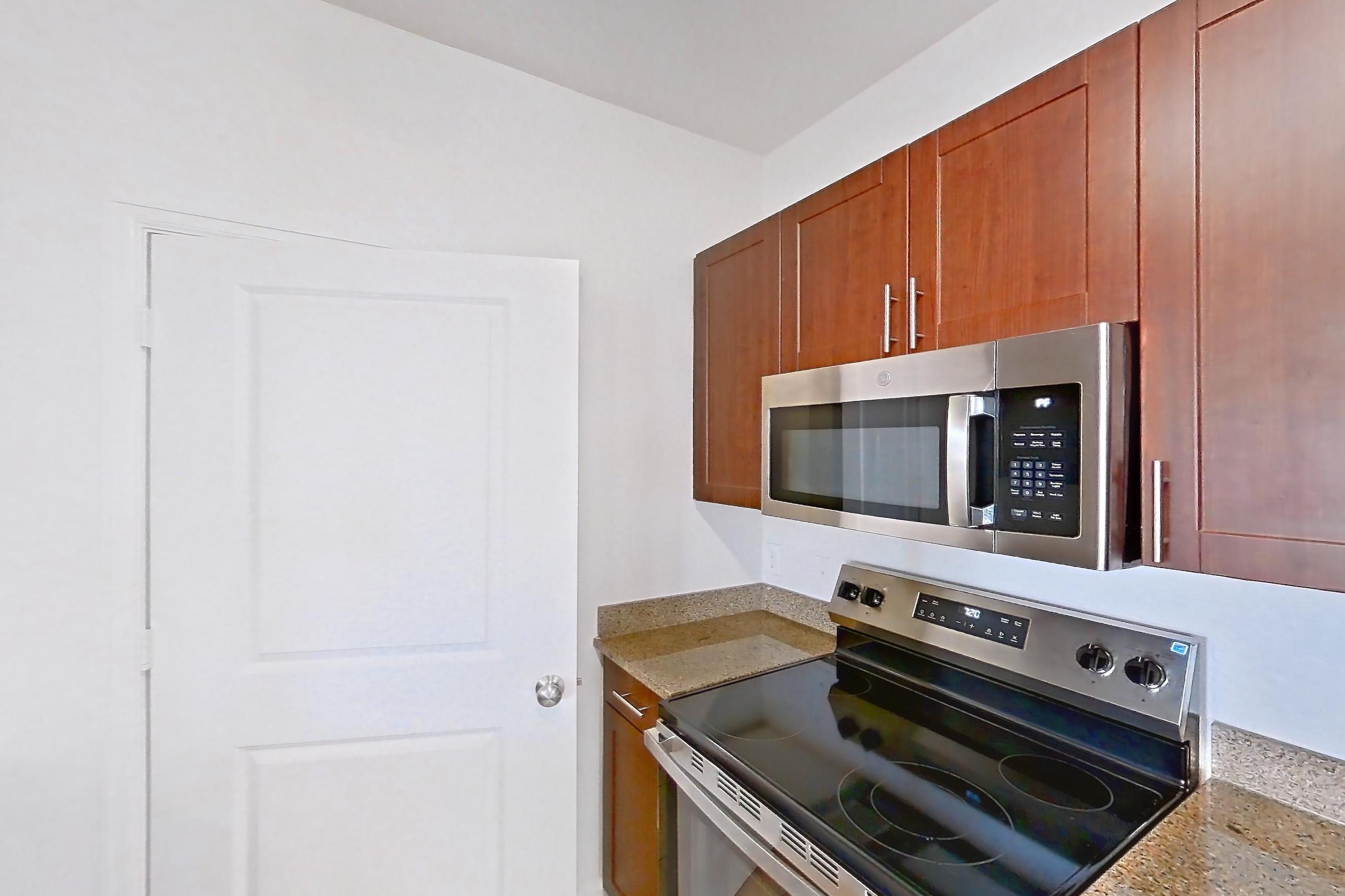 Kitchen with black appliances, dishwasher, electric range, light stone countertops, light tile flooring, light wood-finish flooring, microwave, oven/range, refrigerator, and stainless steel appliances, Apartment 811 at The Cortona
