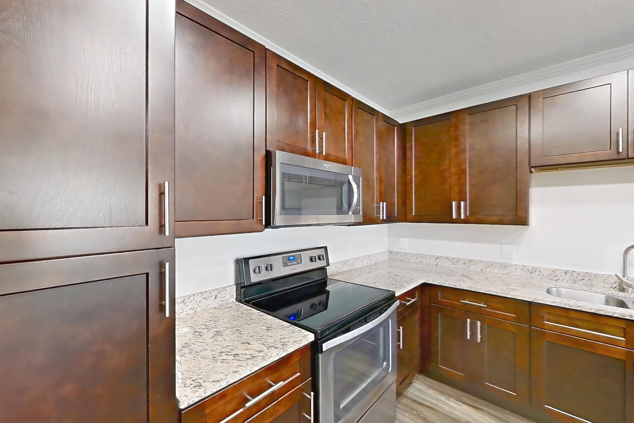 Kitchen with dark wood-finish flooring, dishwasher, electric range, light countertops, light stone countertops, microwave, oven/range, and stainless steel appliances, Apartment 6028 at Lantower Grande Pines