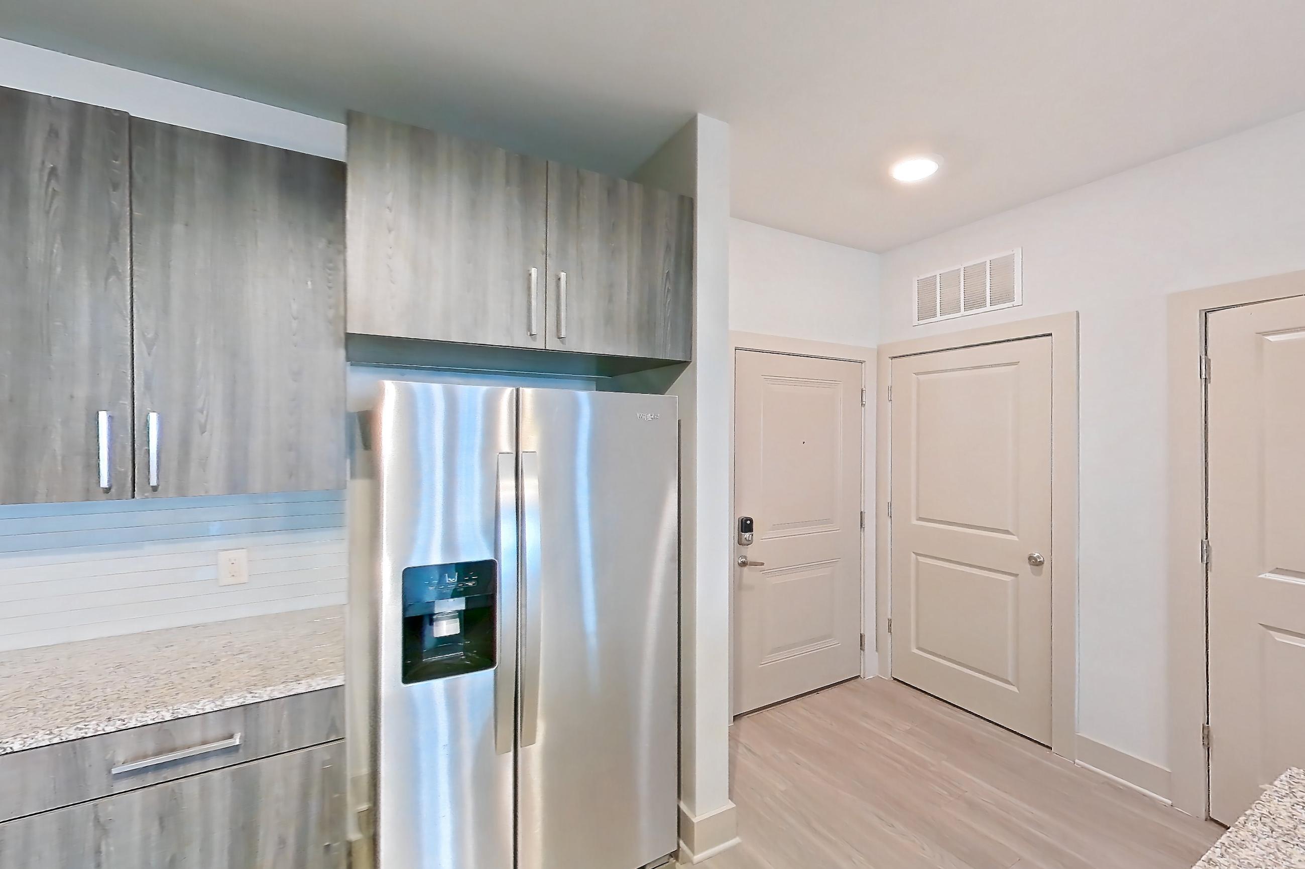 Kitchen with dishwasher, electric range, light countertops, light stone countertops, light wood-finish flooring, microwave, oven/range, refrigerator, stainless steel appliances, and water & ice dispenser, Apartment 11108 at Lantower Waverly