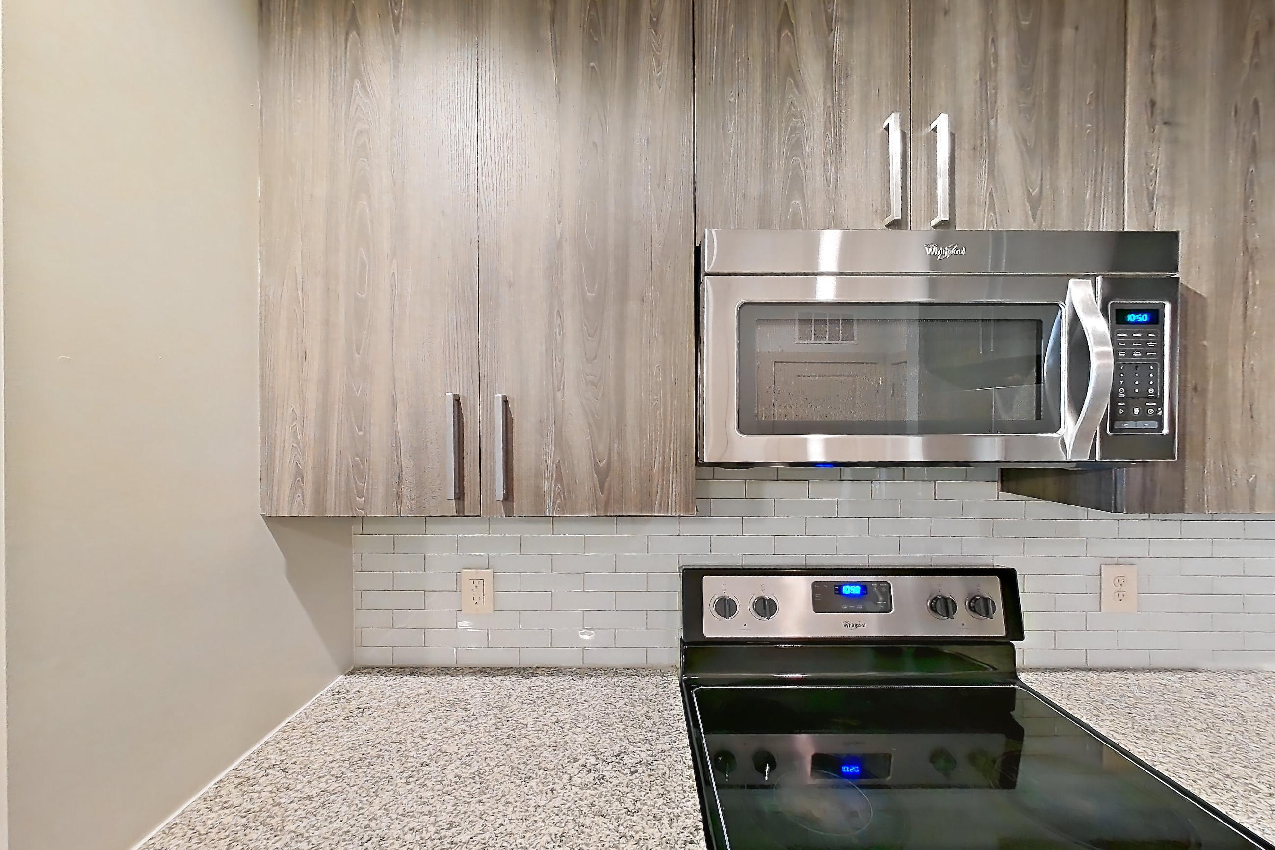 Kitchen with dishwasher, electric range, light countertops, light stone countertops, light wood-finish flooring, microwave, oven/range, refrigerator, stainless steel appliances, and water & ice dispenser, Apartment 11108 at Lantower Waverly