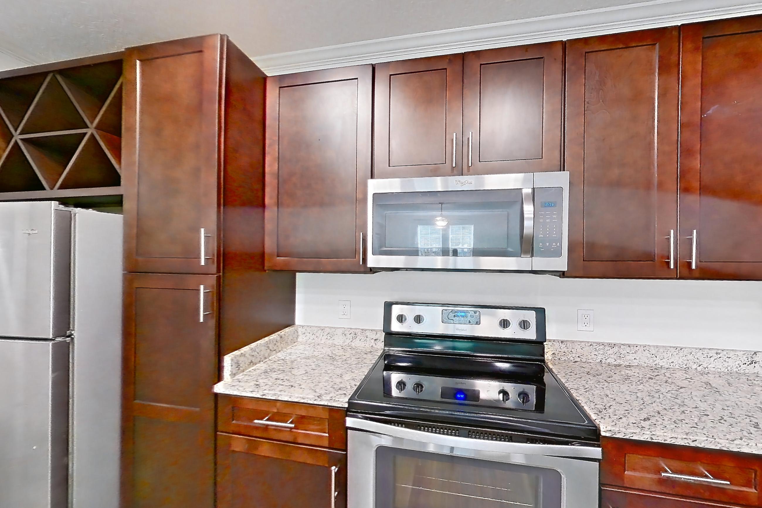 Kitchen with dishwasher, electric range, light stone countertops, light wood-finish flooring, microwave, oven/range, refrigerator, and stainless steel appliances, Apartment 5013 at Lantower Grande Pines