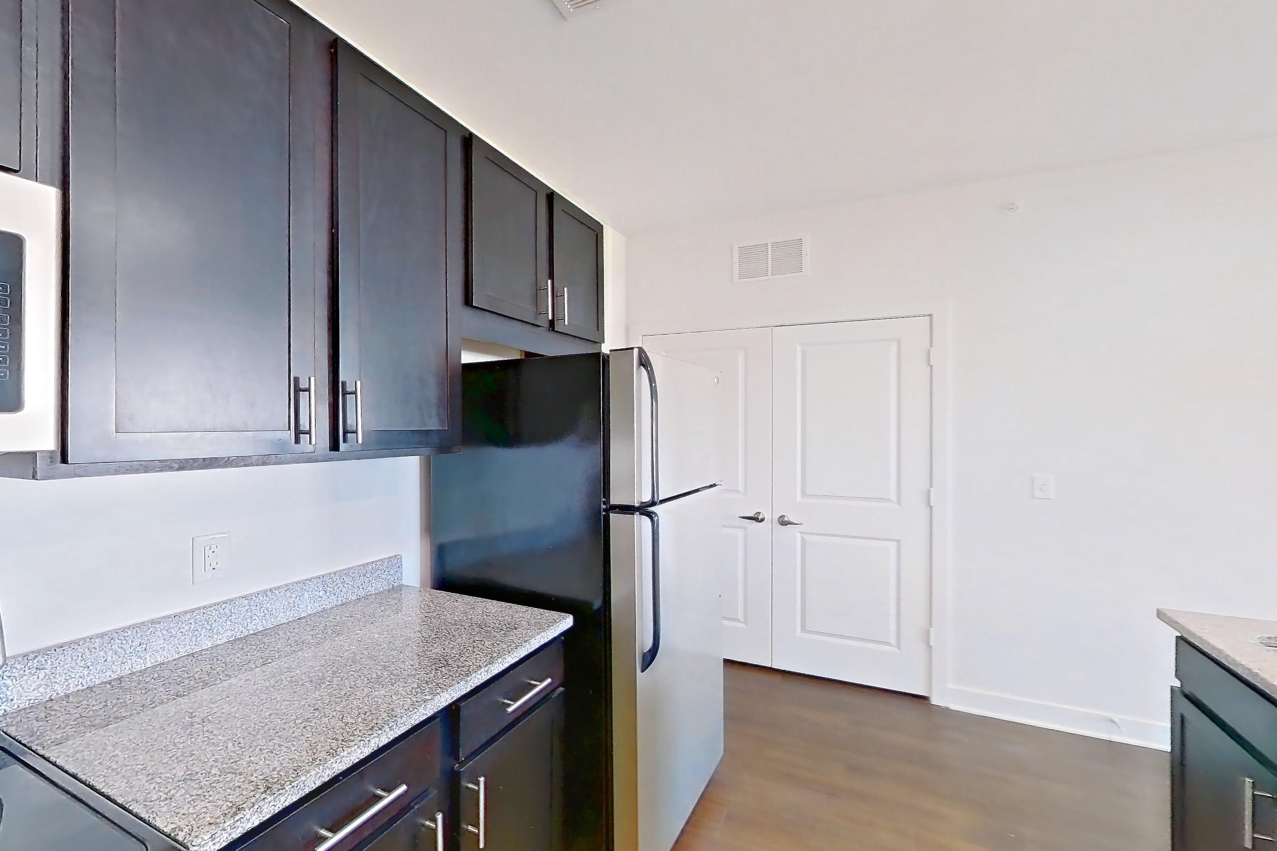 Kitchen with dark wood-finish flooring, dishwasher, electric range, kitchen island, light countertops, light stone countertops, light wood-finish flooring, microwave, oven/range, refrigerator, and stainless steel appliances, Apartment 303 at Realm at Patterson Place