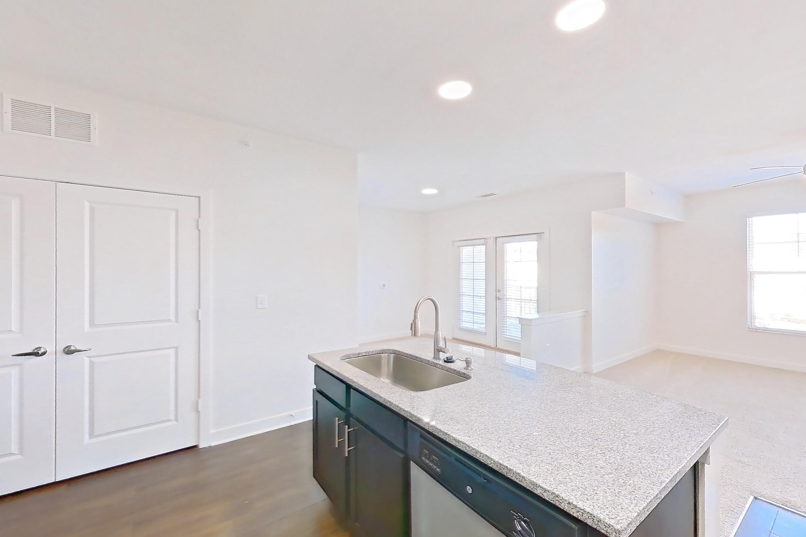 Kitchen with dark wood-finish flooring, dishwasher, electric range, kitchen island, light countertops, light stone countertops, light wood-finish flooring, microwave, oven/range, refrigerator, and stainless steel appliances, Apartment 303 at Realm at Patterson Place