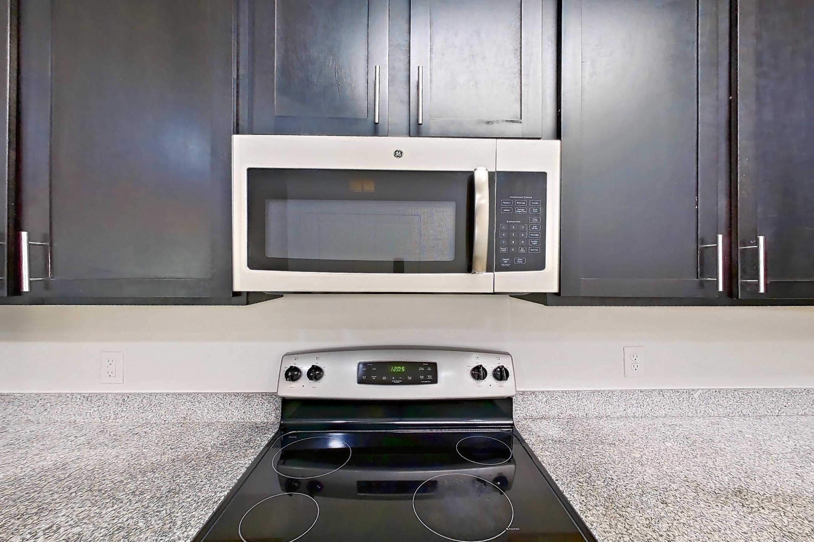 Kitchen with dishwasher, electric range, light countertops, light stone countertops, light wood-finish flooring, microwave, oven/range, refrigerator, and stainless steel appliances, Apartment 008 at Realm at Patterson Place