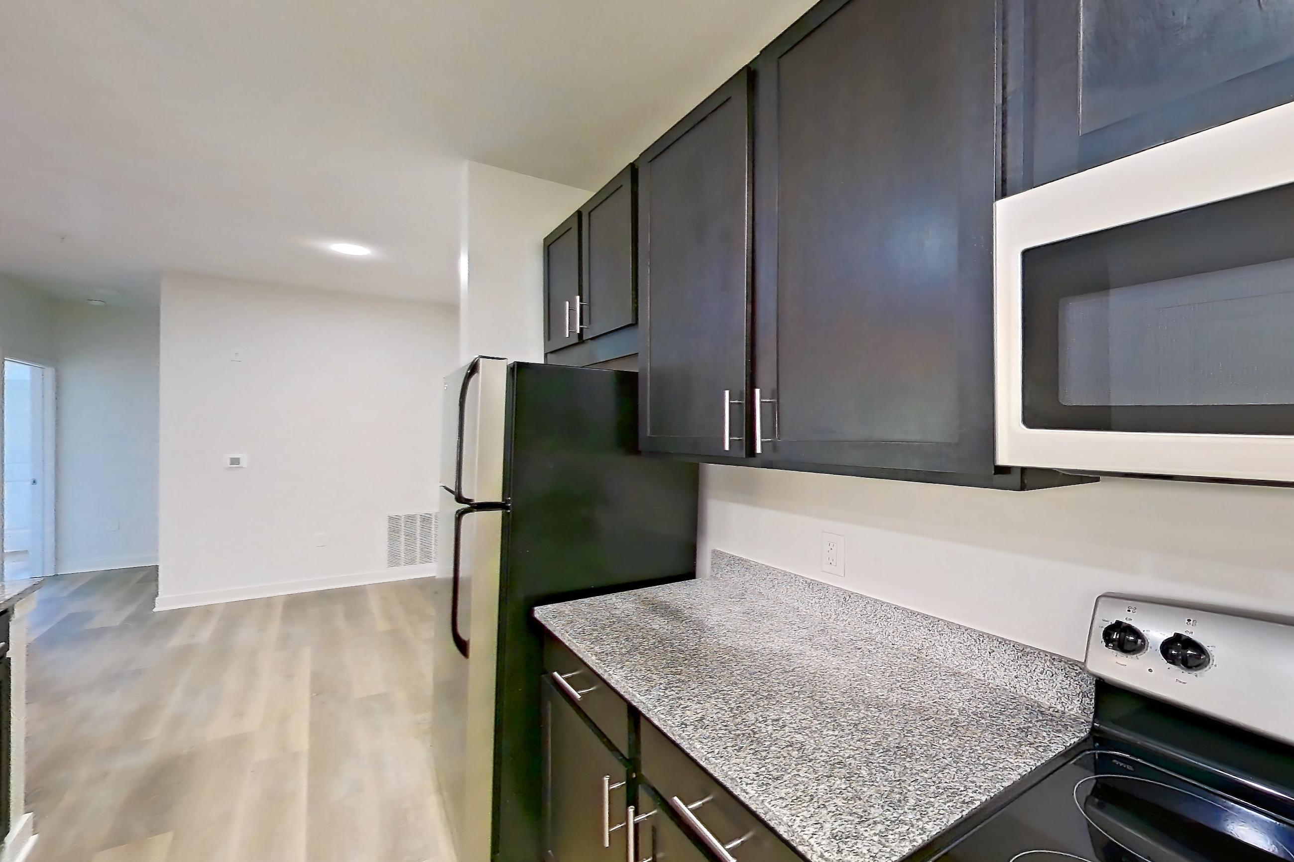 Kitchen with dishwasher, electric range, light countertops, light stone countertops, light wood-finish flooring, microwave, oven/range, refrigerator, and stainless steel appliances, Apartment 008 at Realm at Patterson Place