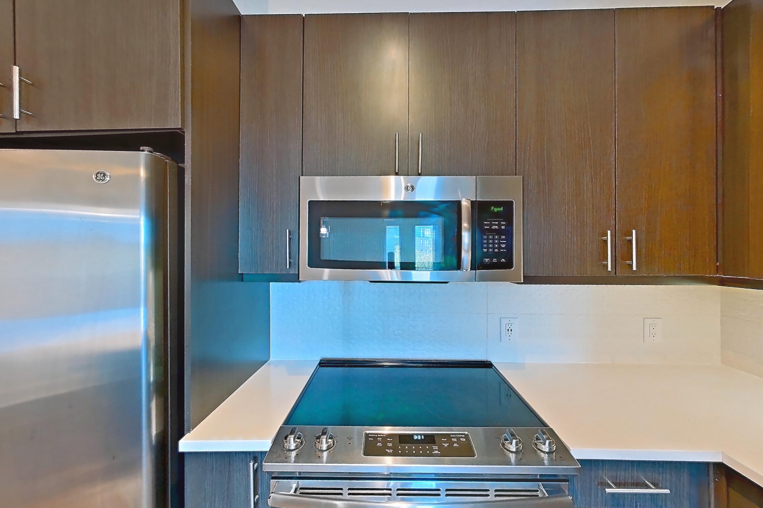 Kitchen with dishwasher, electric range, light countertops, light wood-finish flooring, microwave, oven/range, refrigerator, stainless steel appliances, and water & ice dispenser, Apartment 562 at BullHouse