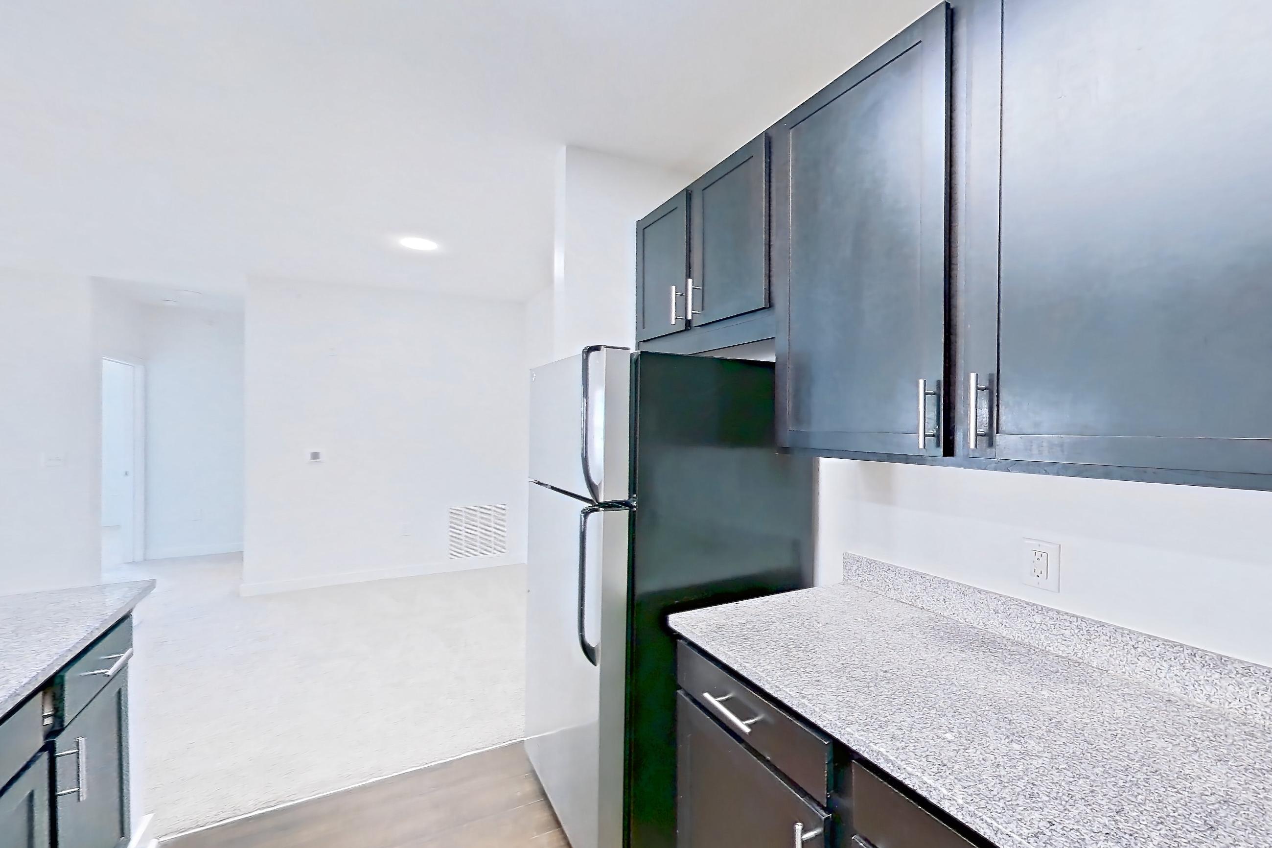Kitchen with dark wood-finish flooring, dishwasher, electric range, light countertops, light stone countertops, light wood-finish flooring, microwave, oven/range, refrigerator, and stainless steel appliances, Apartment 208 at Realm at Patterson Place