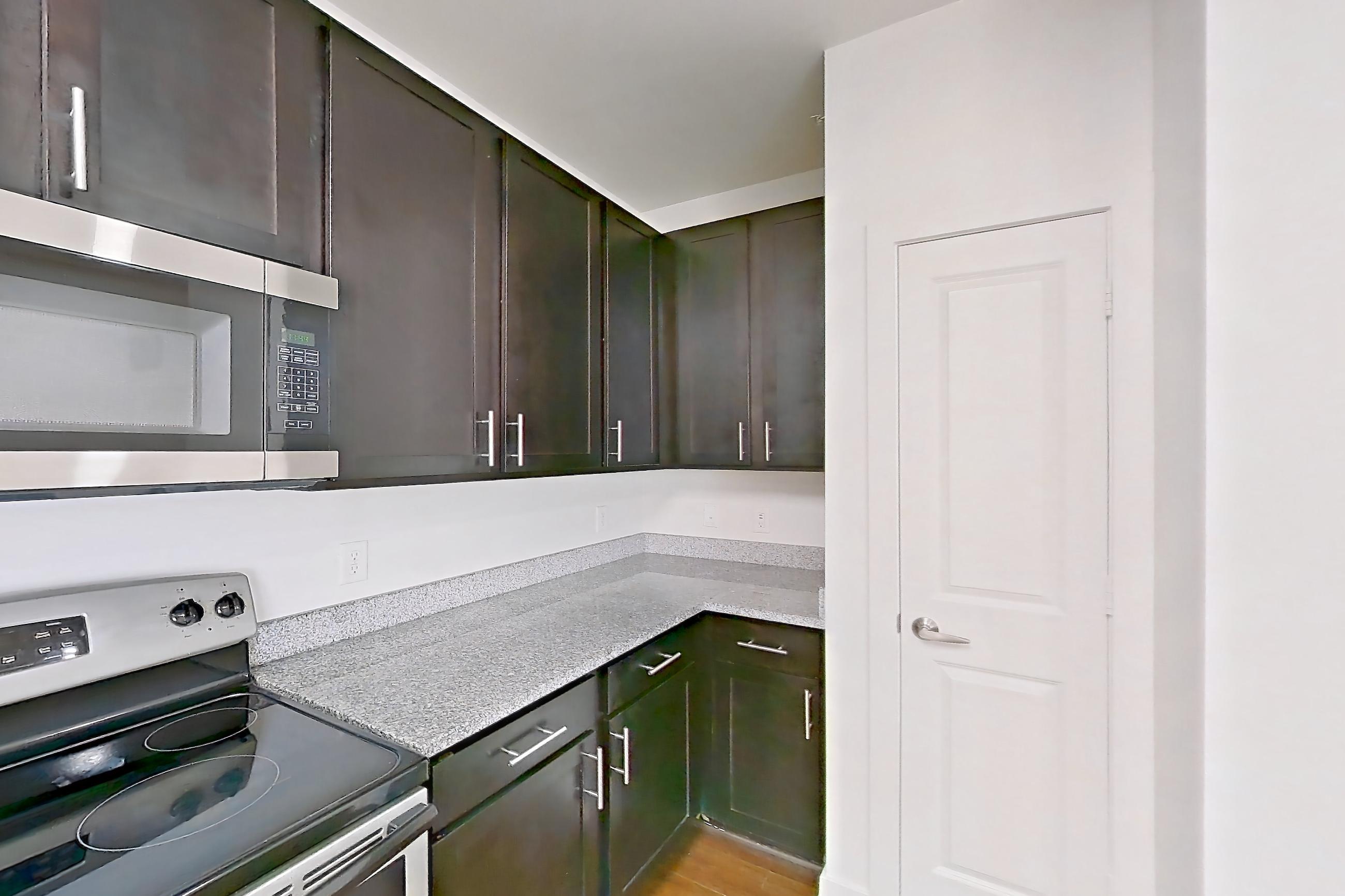 Kitchen with dark wood-finish flooring, dishwasher, electric range, light countertops, light stone countertops, light wood-finish flooring, microwave, oven/range, refrigerator, and stainless steel appliances, Apartment 301 at Realm at Patterson Place