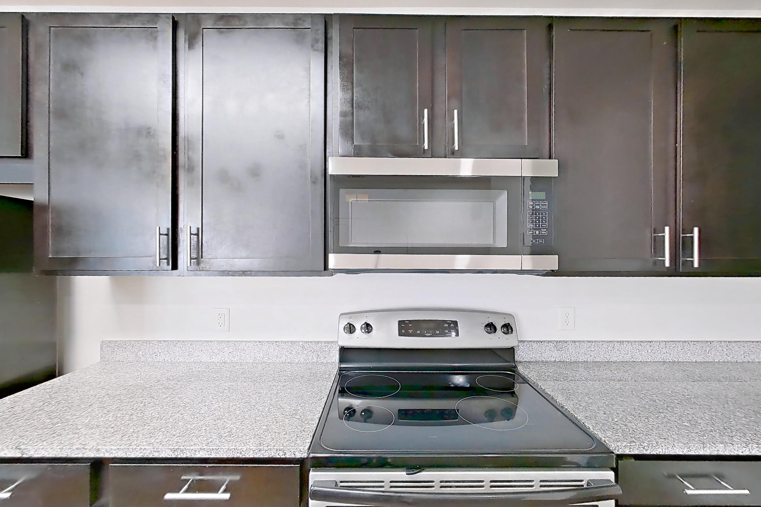 Kitchen with dark wood-finish flooring, dishwasher, electric range, light countertops, light stone countertops, light wood-finish flooring, microwave, oven/range, refrigerator, and stainless steel appliances, Apartment 301 at Realm at Patterson Place