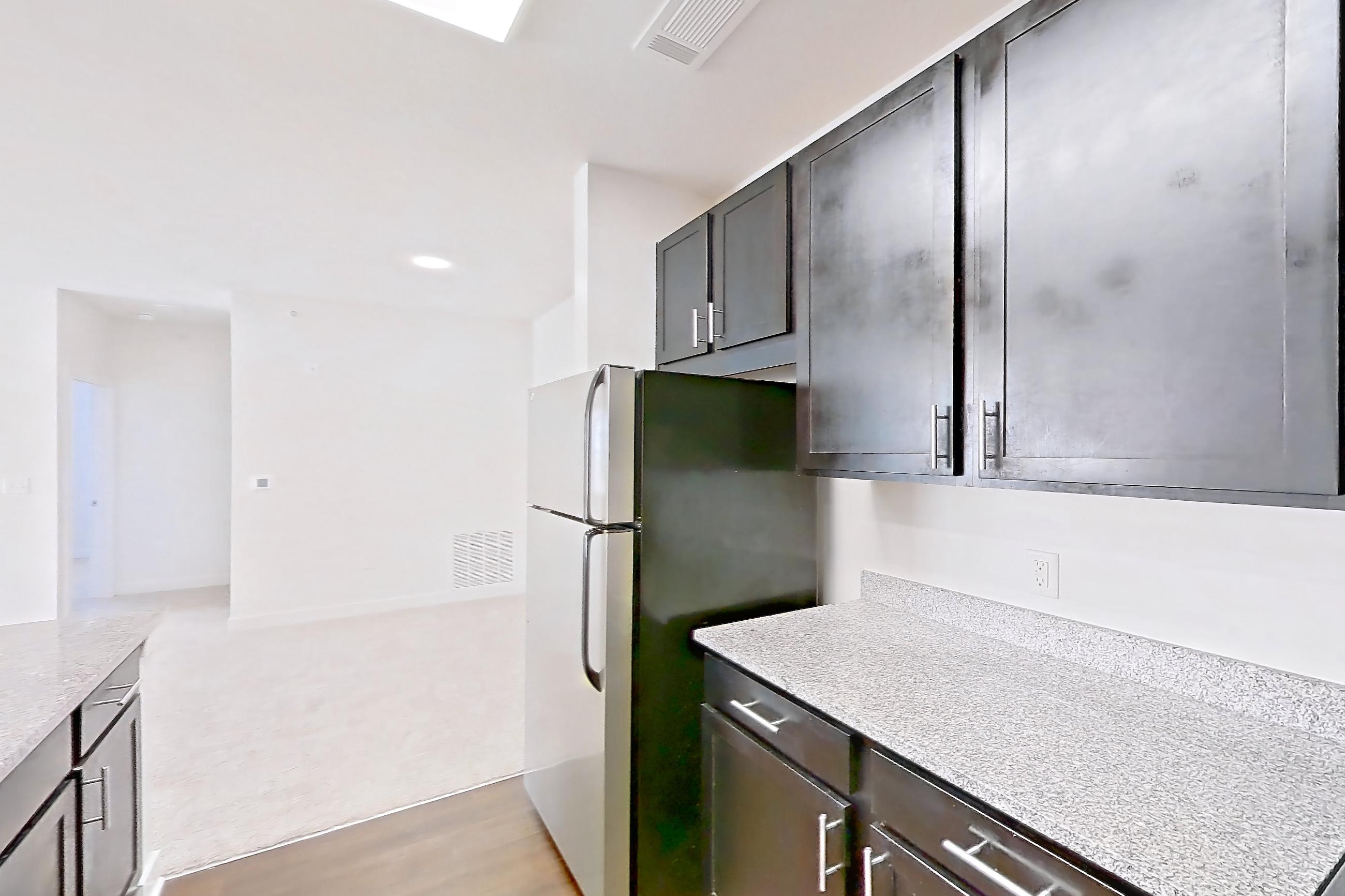 Kitchen with dark wood-finish flooring, dishwasher, electric range, light countertops, light stone countertops, light wood-finish flooring, microwave, oven/range, refrigerator, and stainless steel appliances, Apartment 301 at Realm at Patterson Place