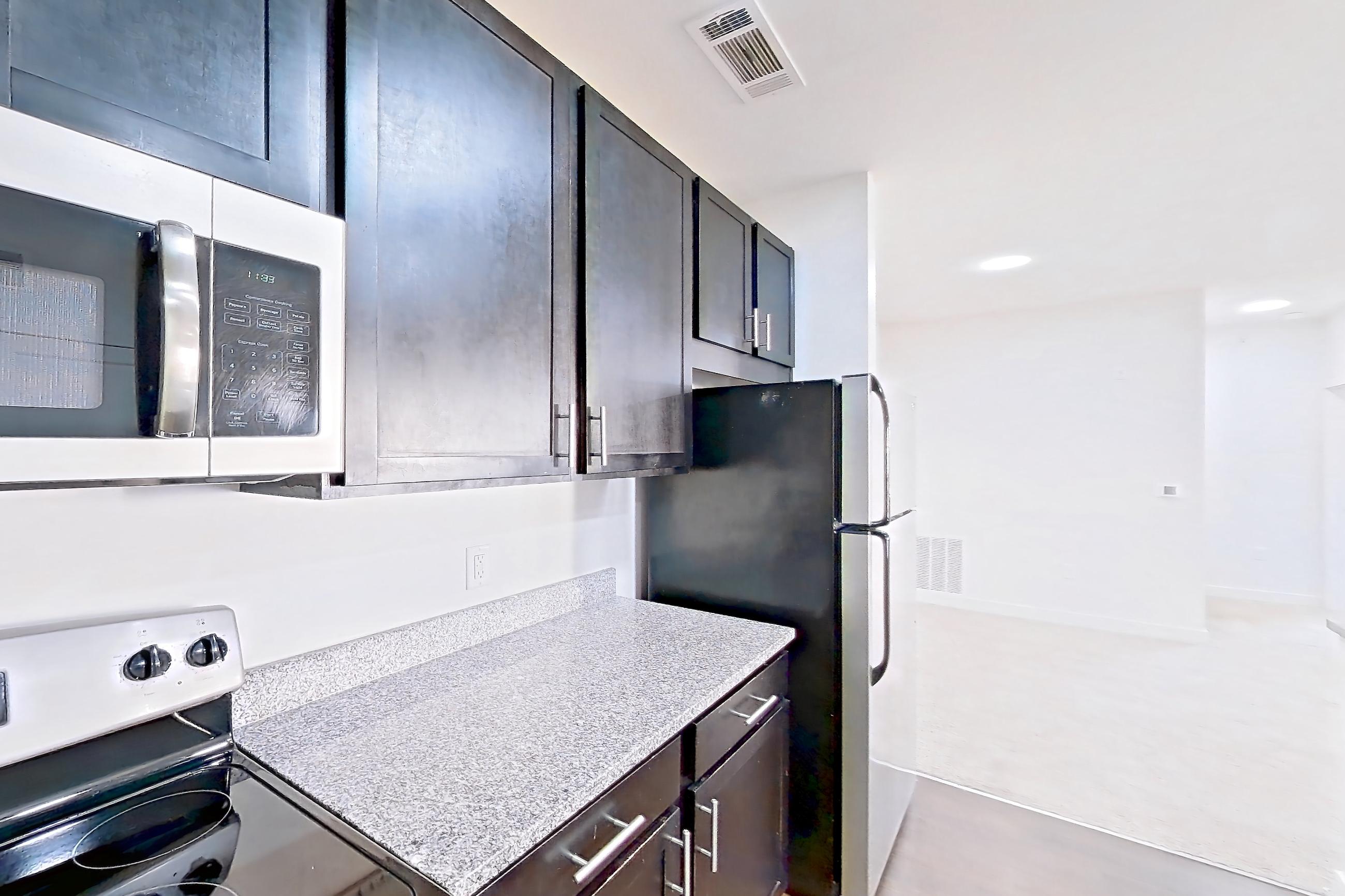 Kitchen with dark wood-finish flooring, dishwasher, electric range, light countertops, light stone countertops, microwave, oven/range, refrigerator, and stainless steel appliances, Apartment 302 at Realm at Patterson Place