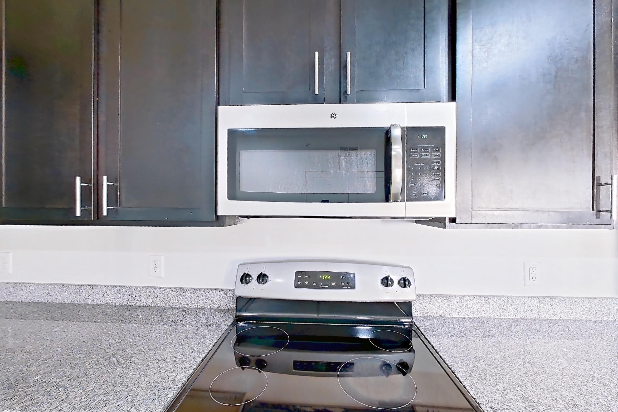 Kitchen with dark wood-finish flooring, dishwasher, electric range, light countertops, light stone countertops, microwave, oven/range, refrigerator, and stainless steel appliances, Apartment 302 at Realm at Patterson Place
